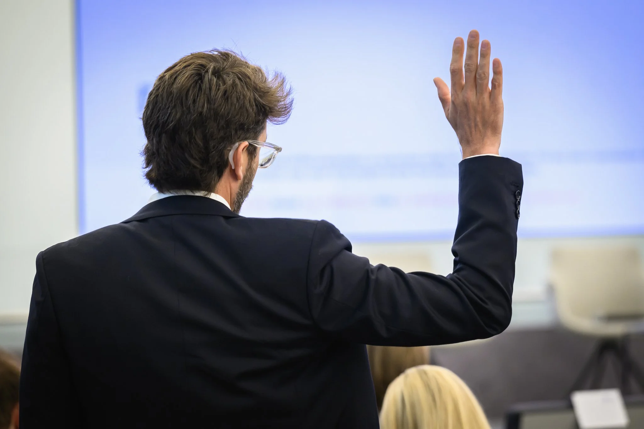 A man seen from behind raises his hand during a conference session.