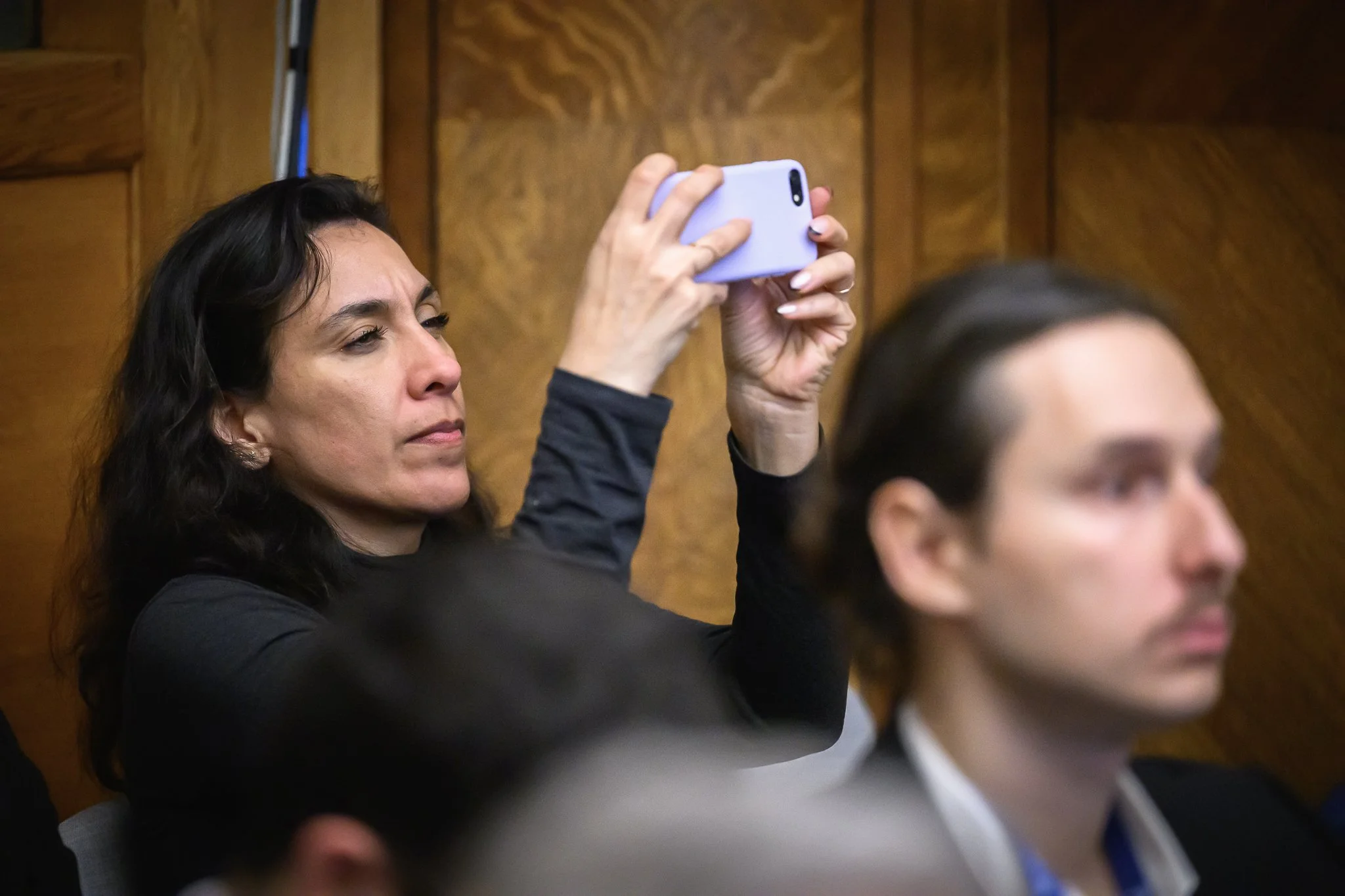 A seated participant holds up a smartphone to photograph the presentation.
