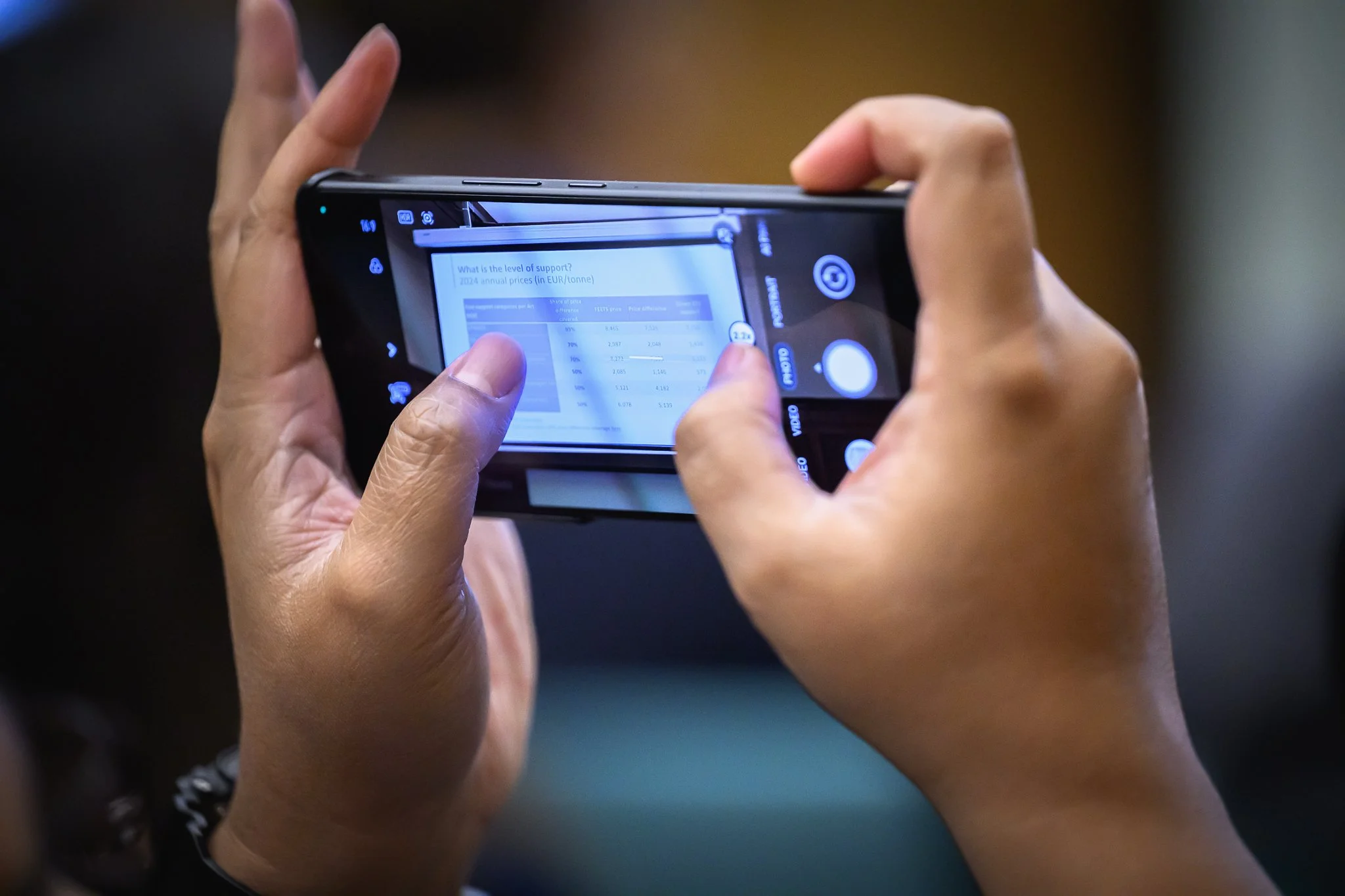 Close-up of hands holding a smartphone horizontally to photograph a presentation slide.