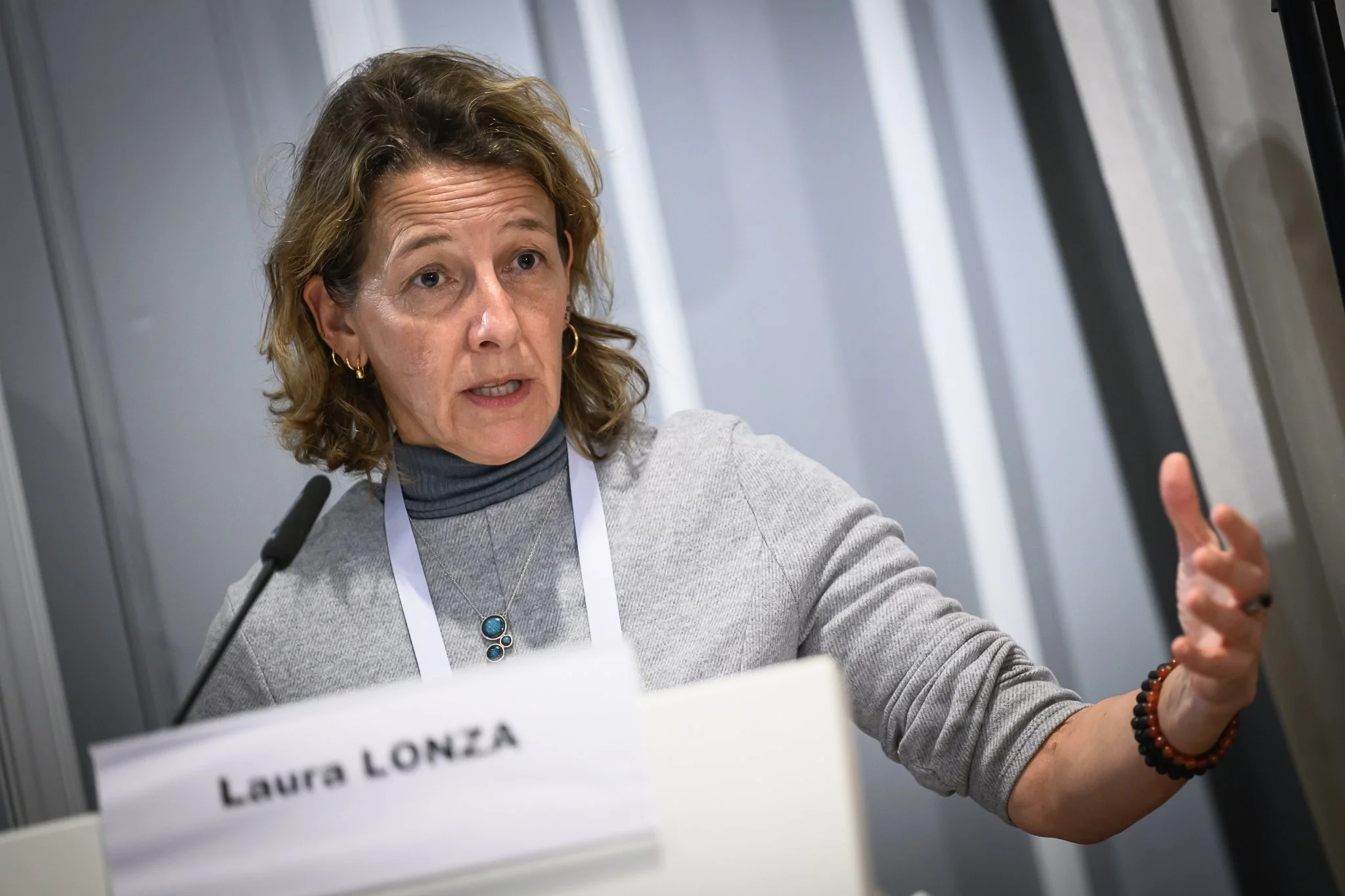 Laura Lonza extends one hand while speaking into the lectern microphone.
