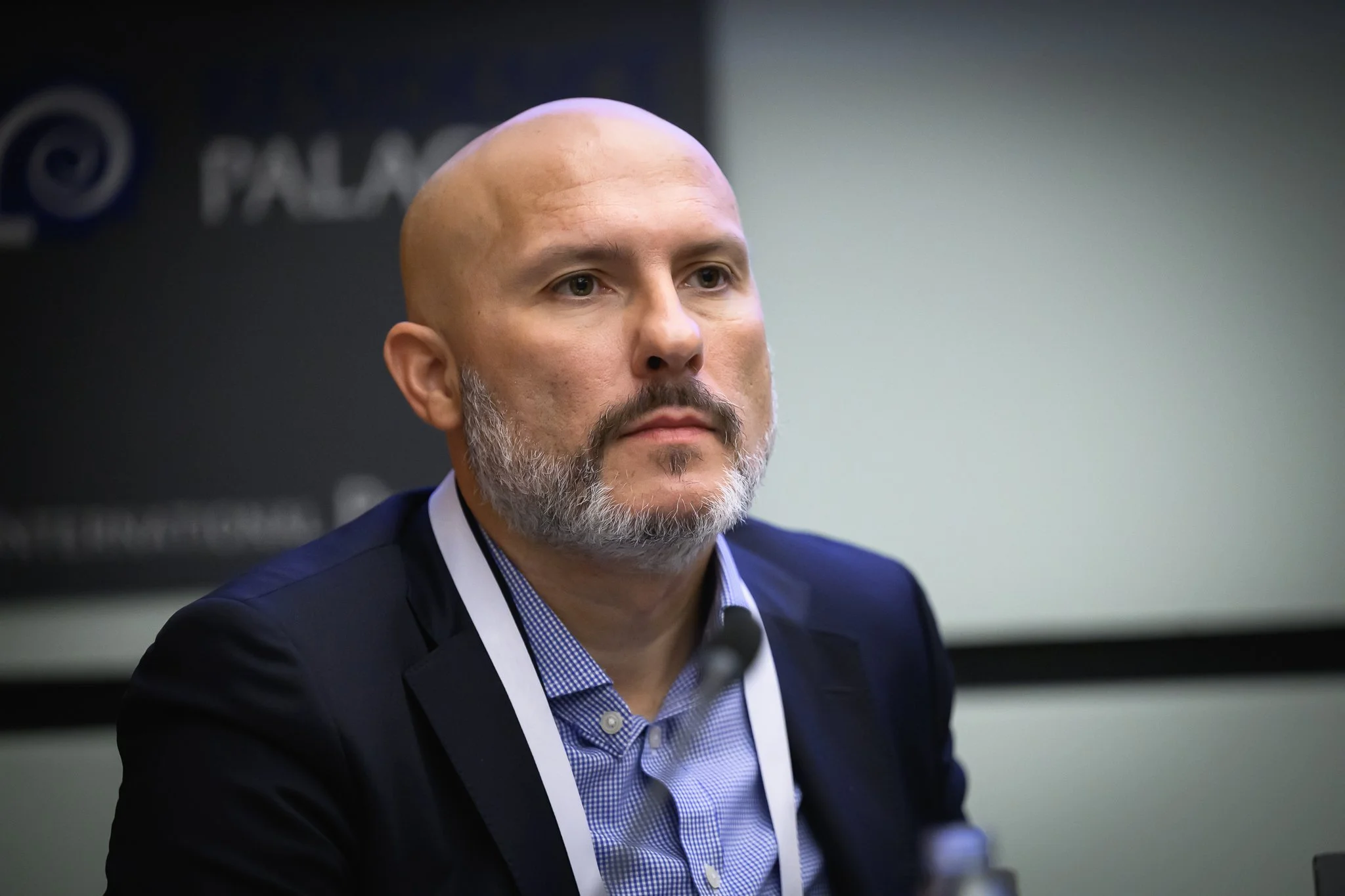A bald man with a grey beard listens during a conference session.