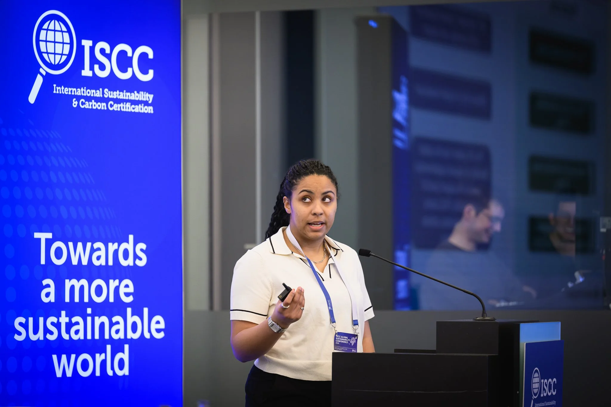 A woman in a light blouse gestures with a presentation remote at the lectern.