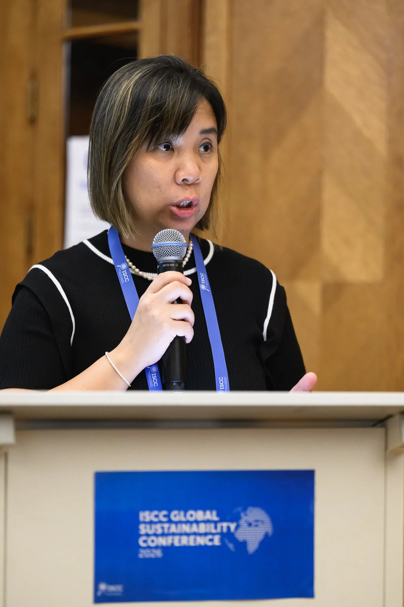 A woman in a black top speaks into a handheld microphone behind a lectern.