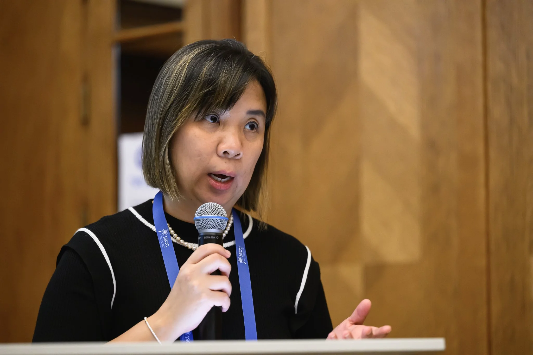 A woman gestures with one hand while speaking into a microphone.