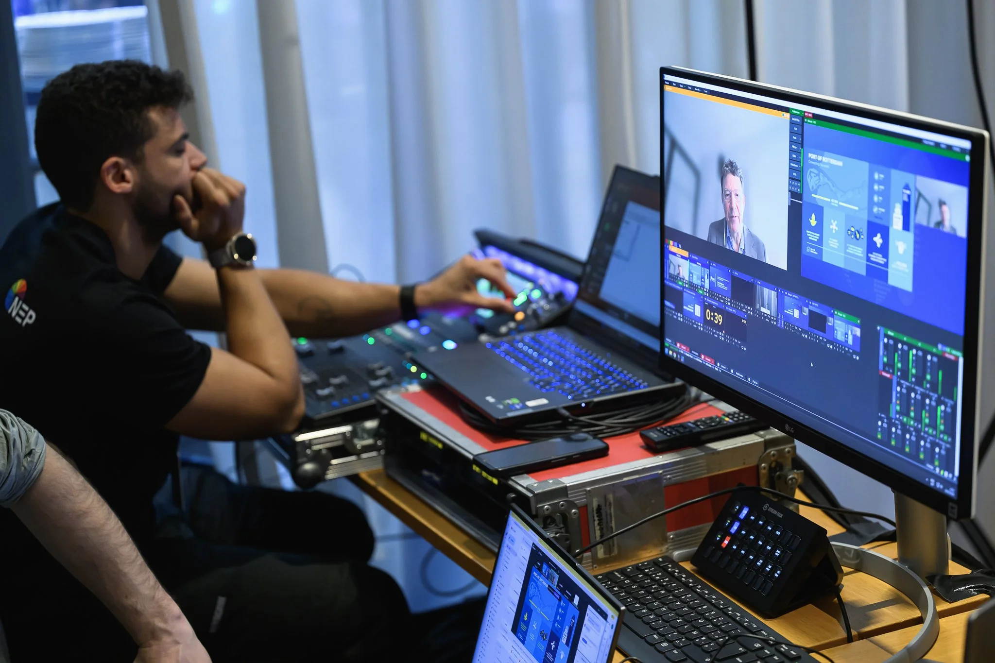 A technician operates video production equipment beside monitors showing the conference feed.
