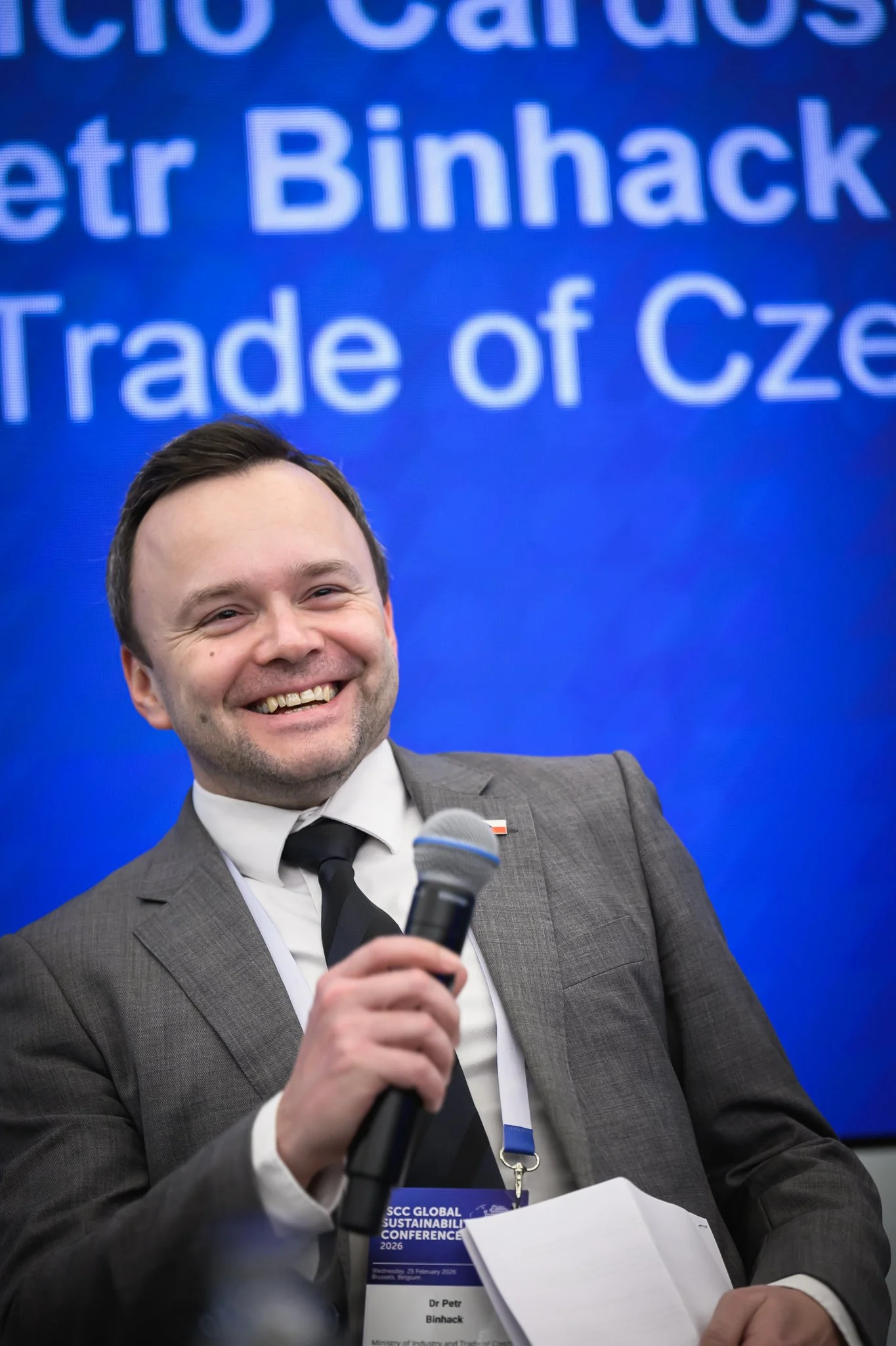 A smiling man in a grey suit holds a microphone during a panel discussion.