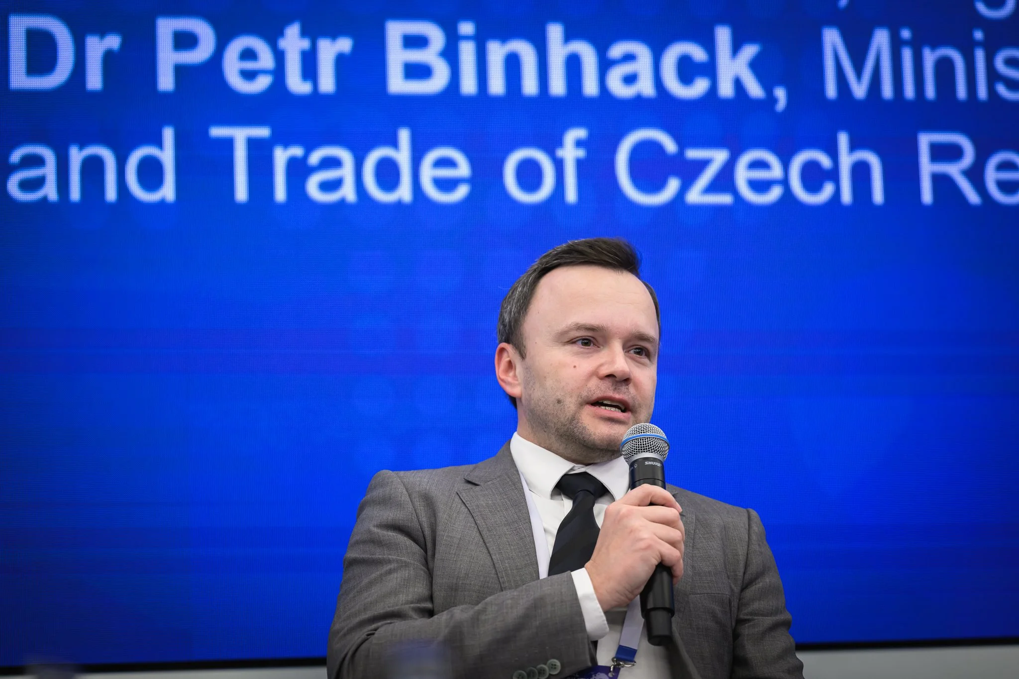 A man in a grey suit speaks into a microphone during the panel discussion.