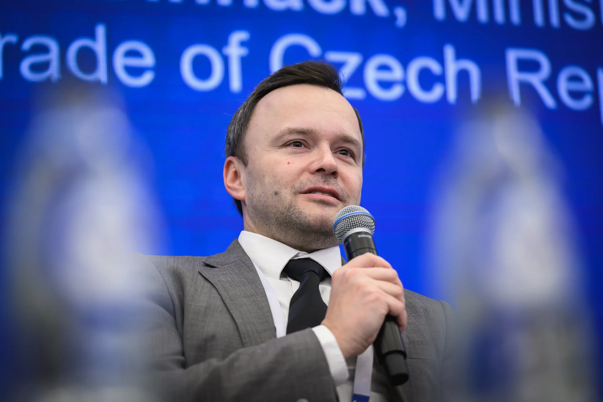 Close-up of a panel participant speaking into a microphone against a blue backdrop.