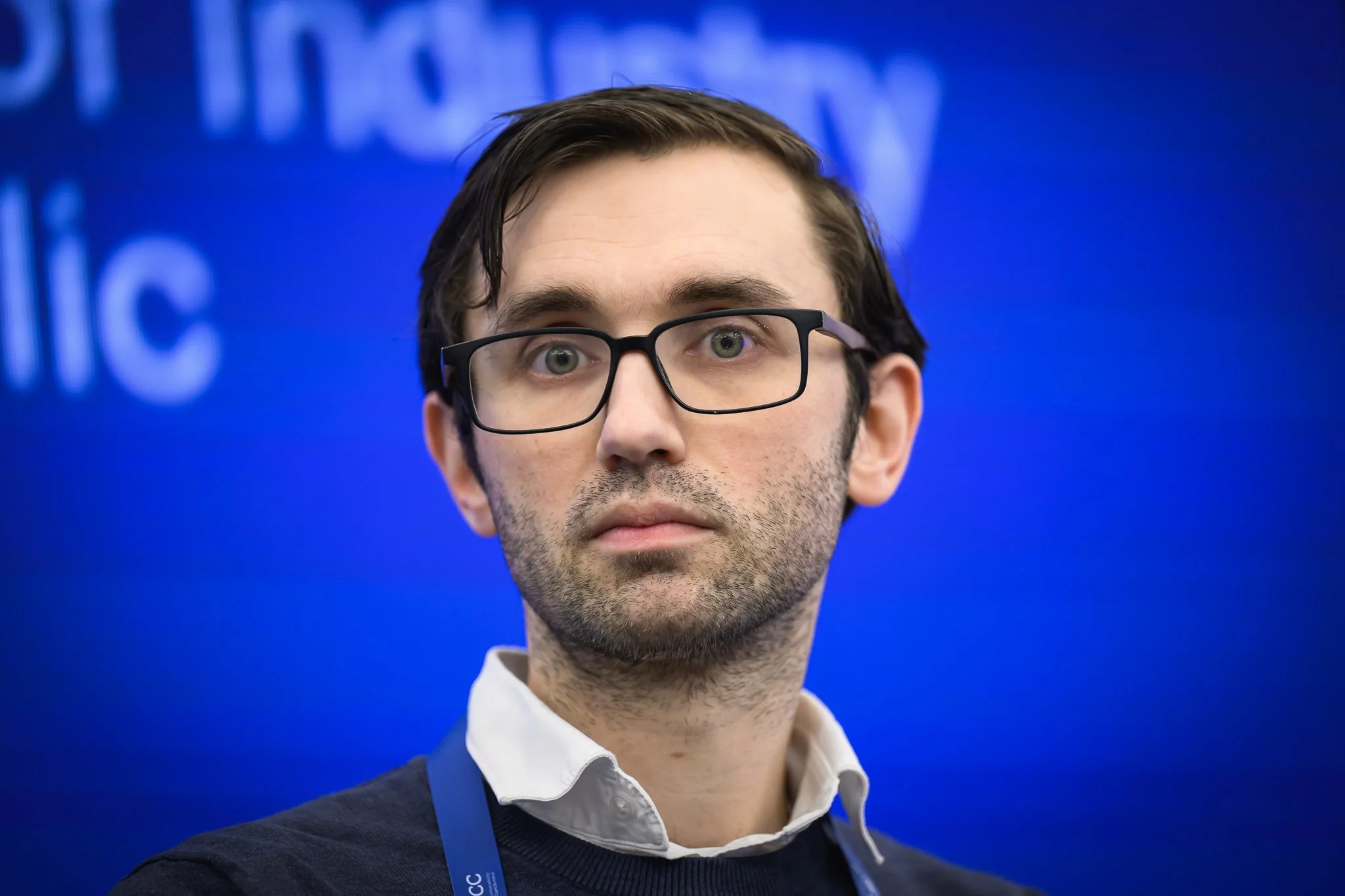A man with glasses listens during a panel discussion.