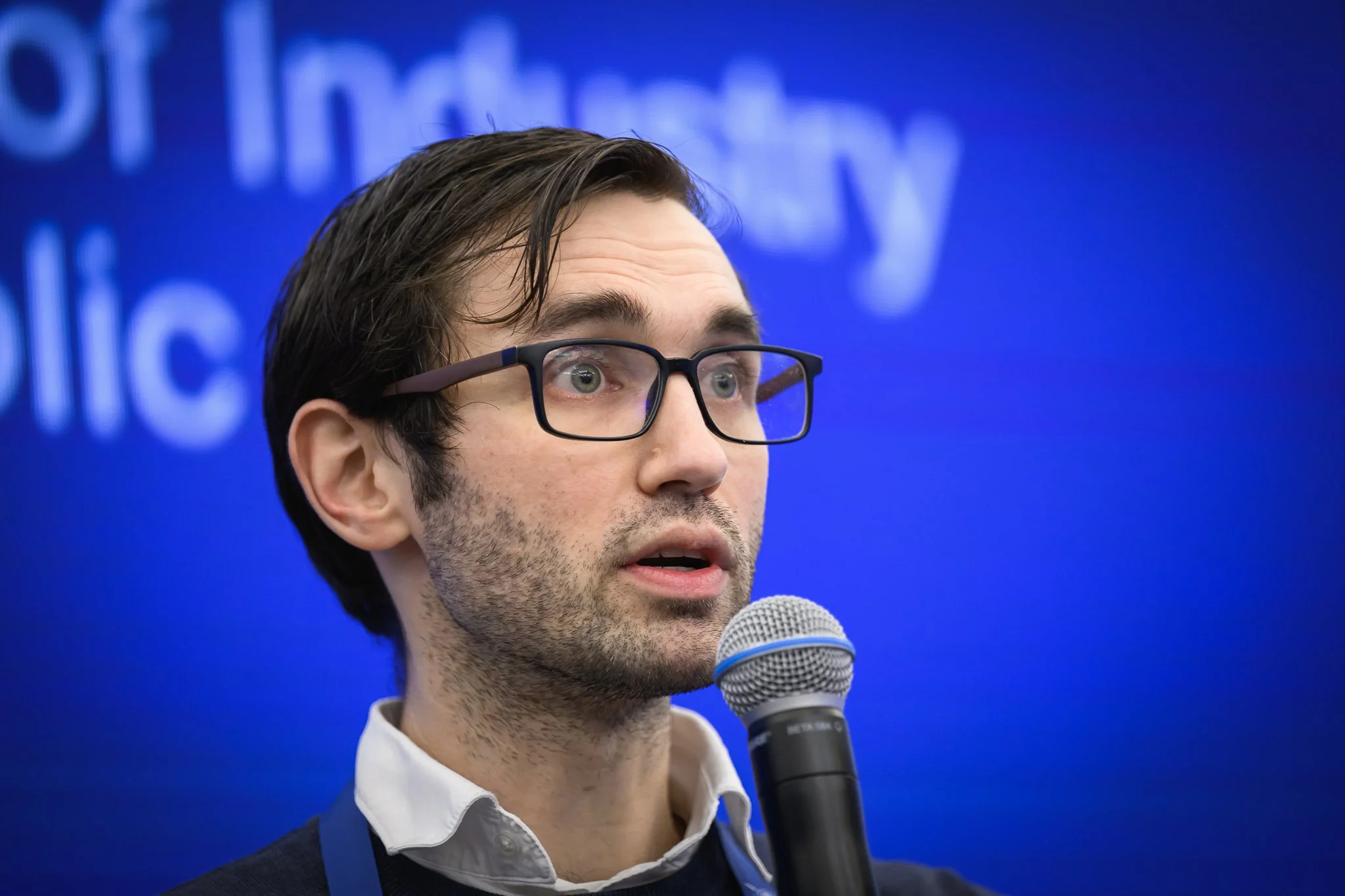 Close-up of a man with glasses speaking into a handheld microphone.