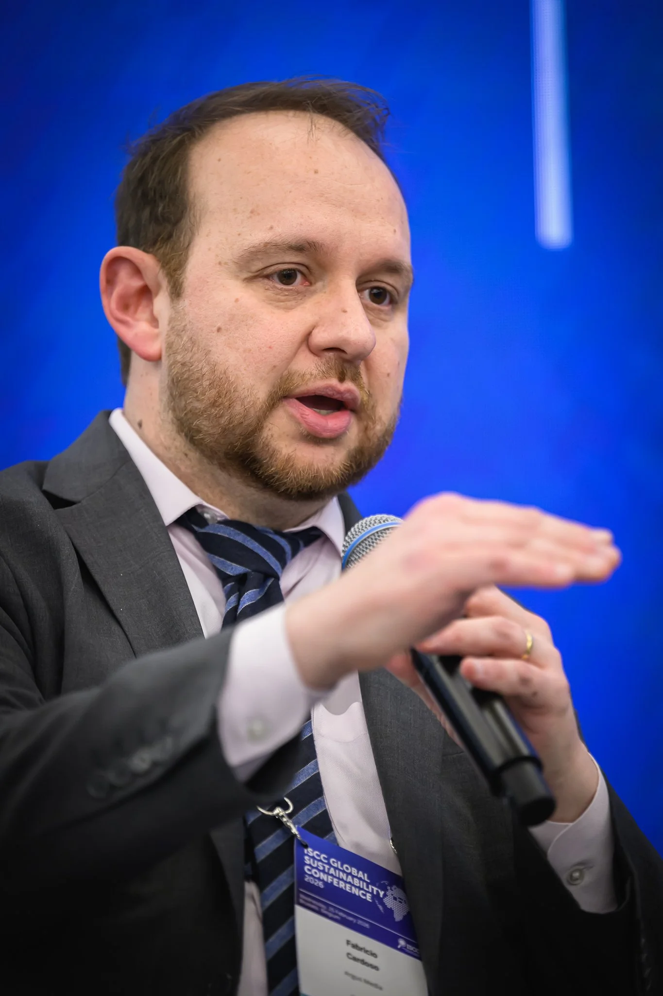 A seated panel participant gestures with one hand while holding a microphone.