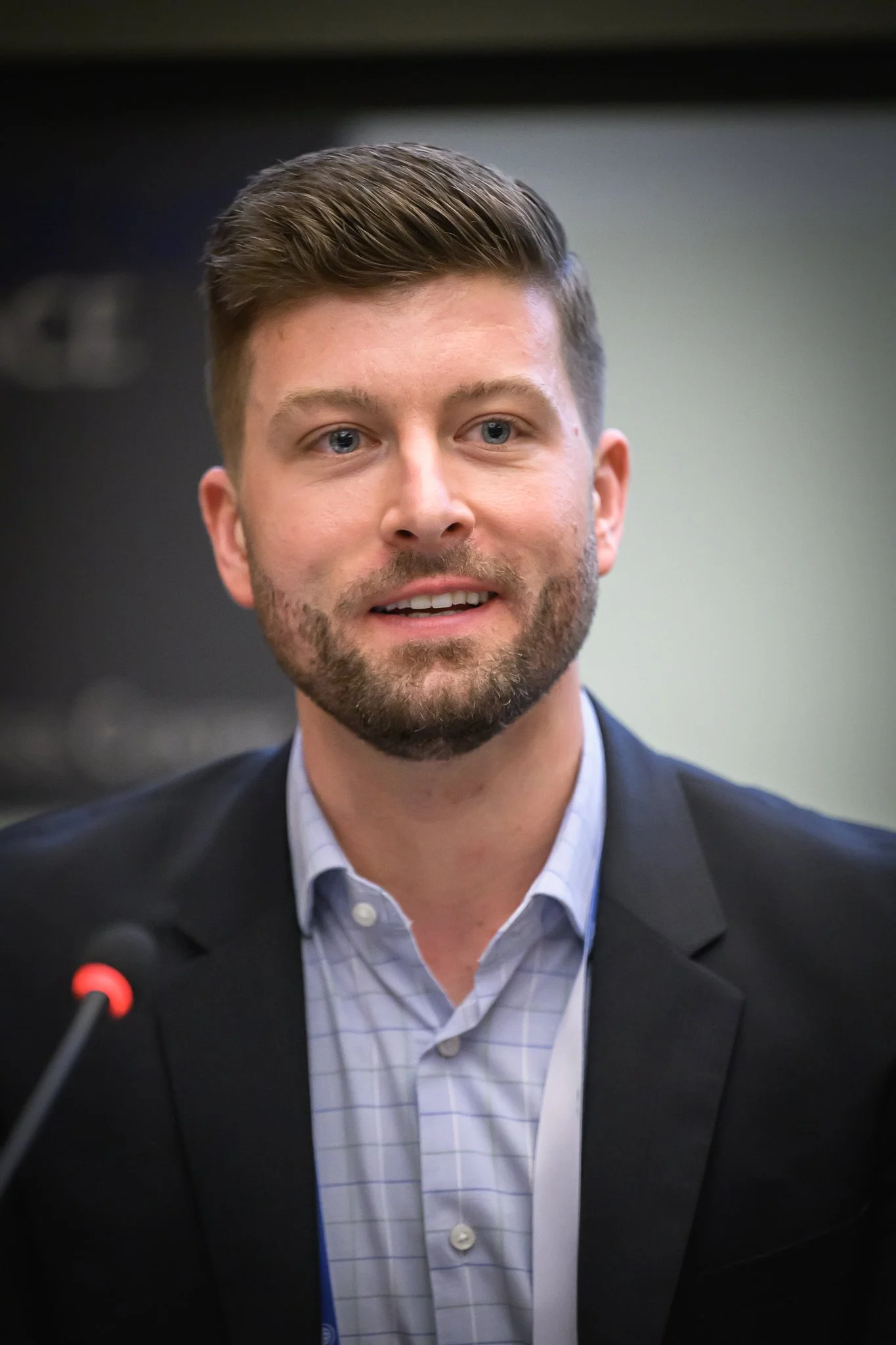 A bearded man listens from his seat at a conference table.