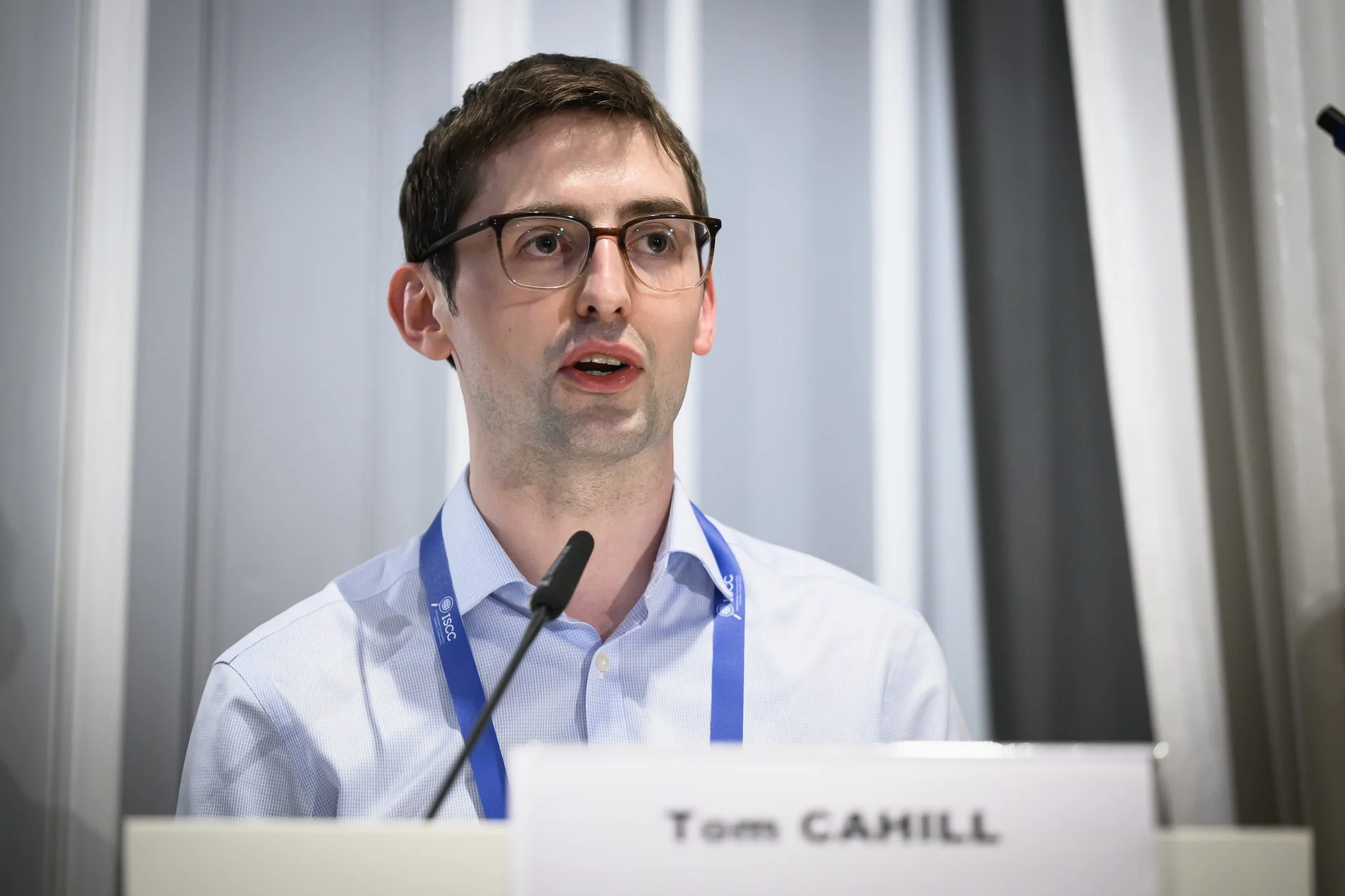 Tom Cahill speaks at a lectern bearing his name.