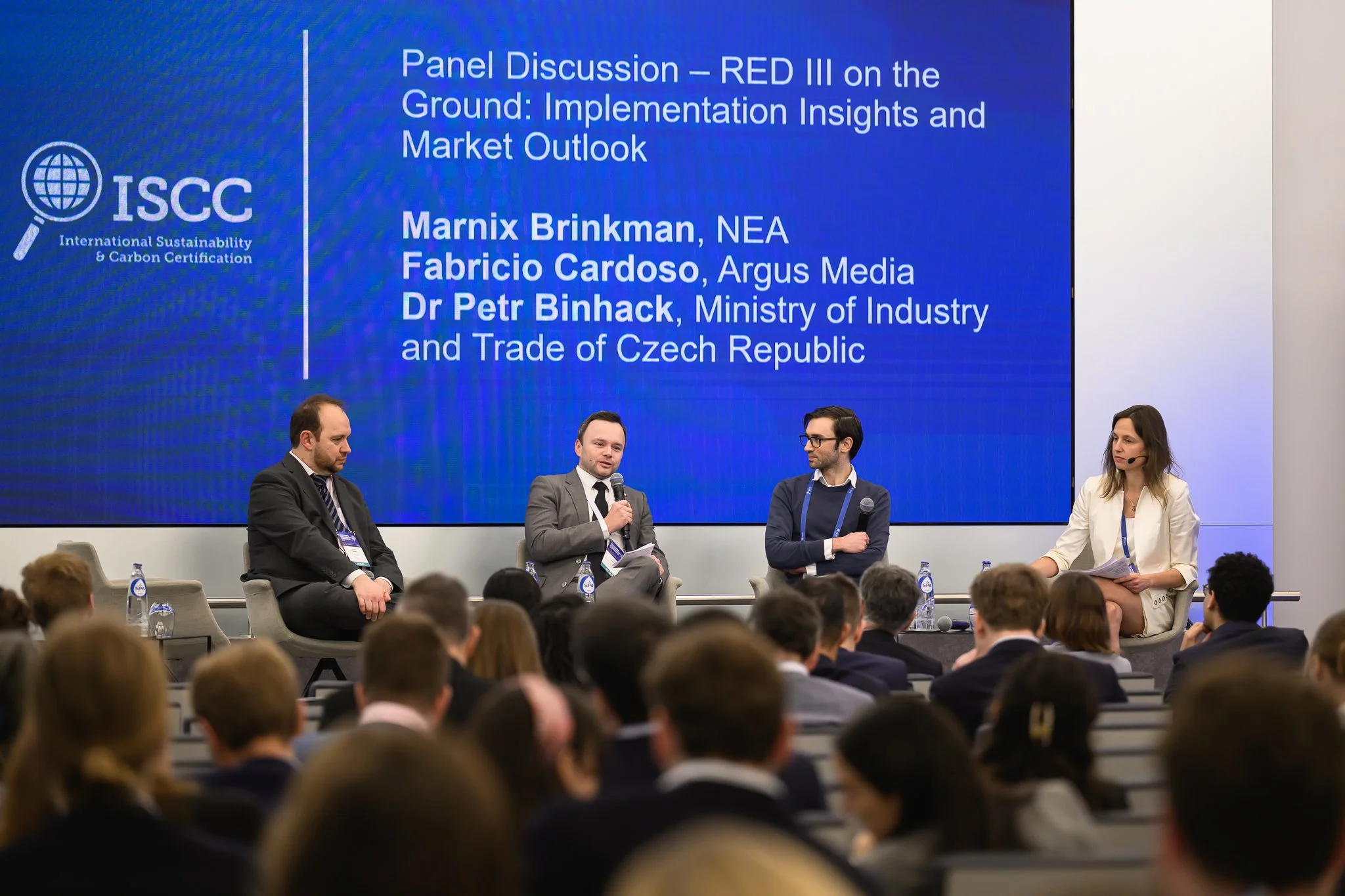 Four panel participants sit on stage beneath a screen about RED III implementation and market outlook.
