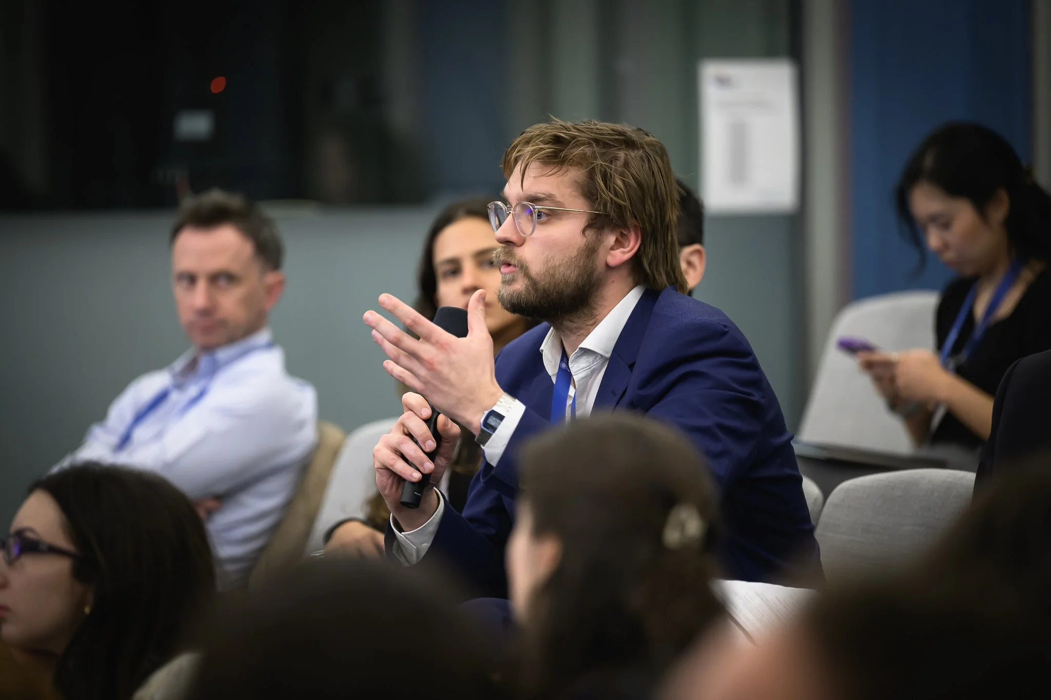 A man in the audience gestures while asking a question with a handheld microphone.