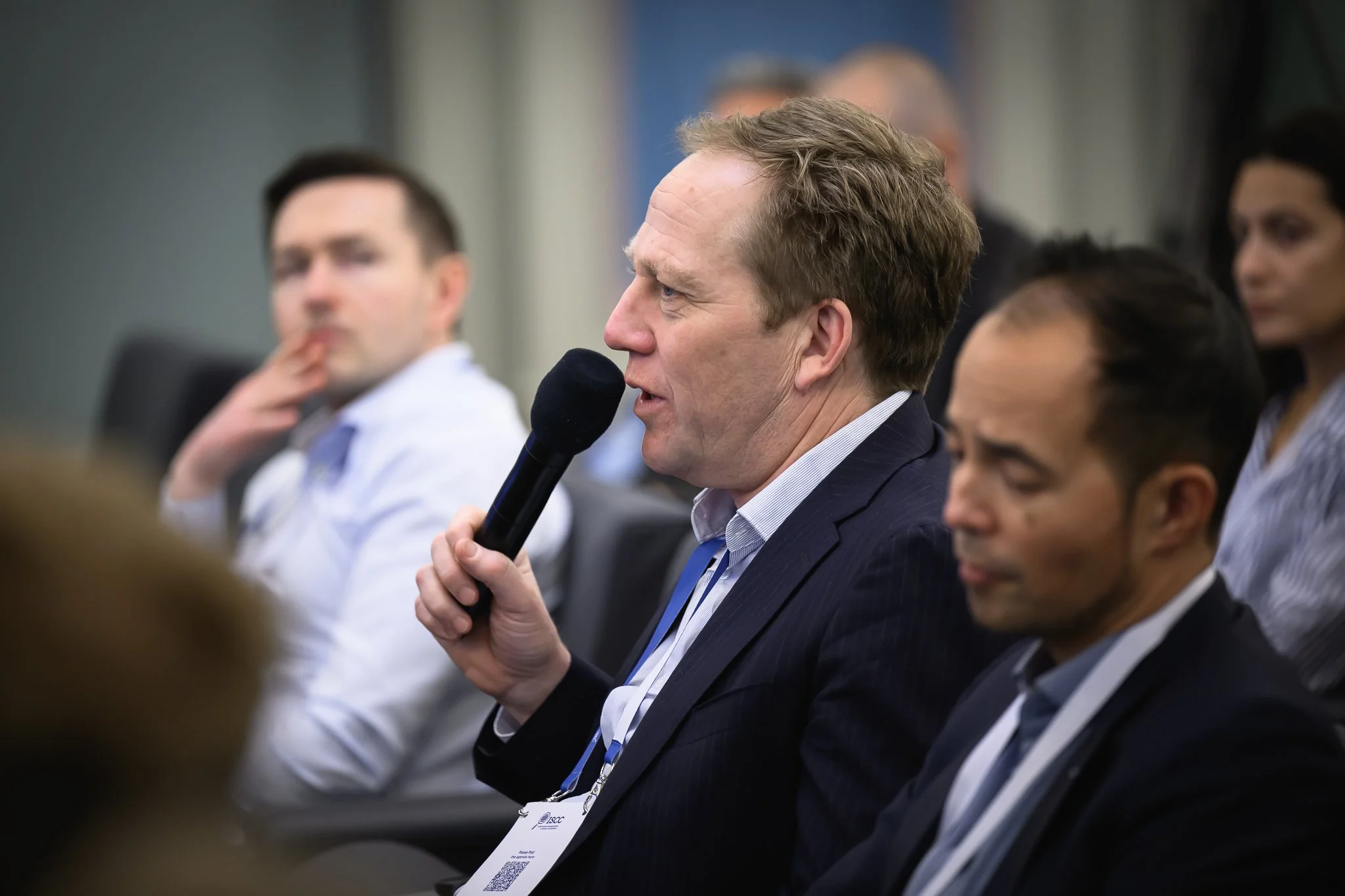 A seated man asks a question using a handheld microphone.