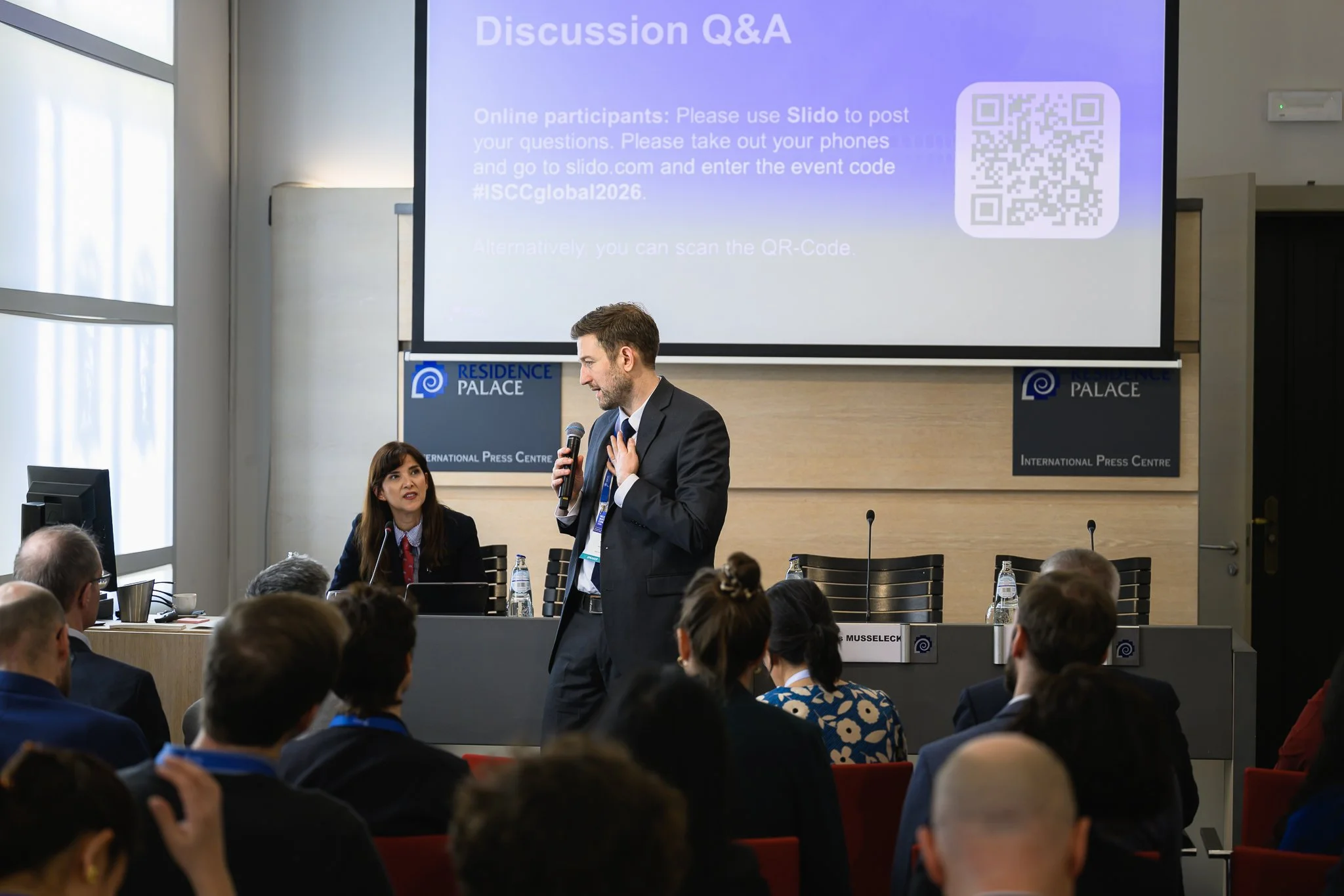 A speaker addresses the audience beneath a Discussion Q&A slide with a QR code.