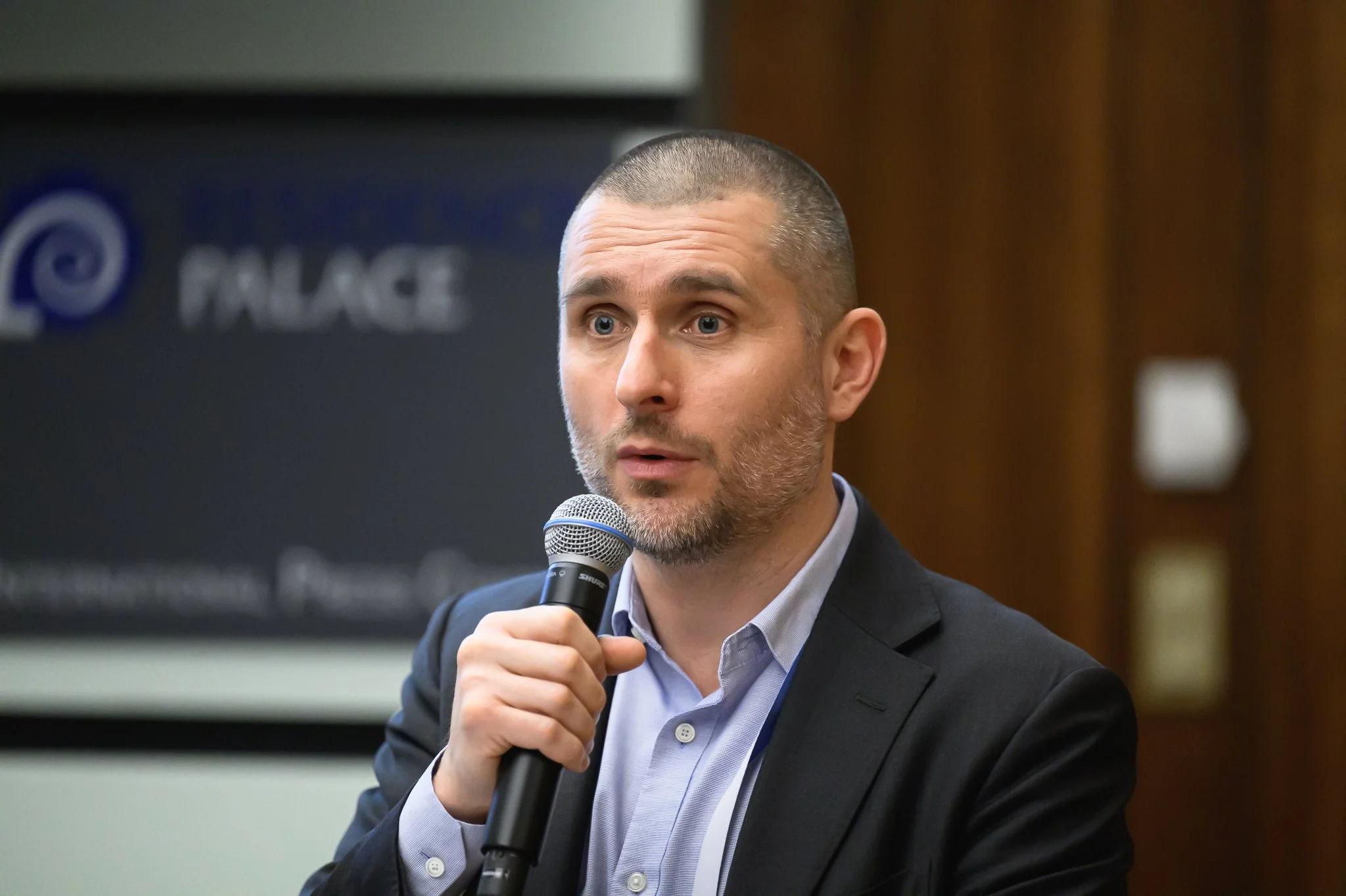 A man with closely cropped hair speaks into a handheld microphone.