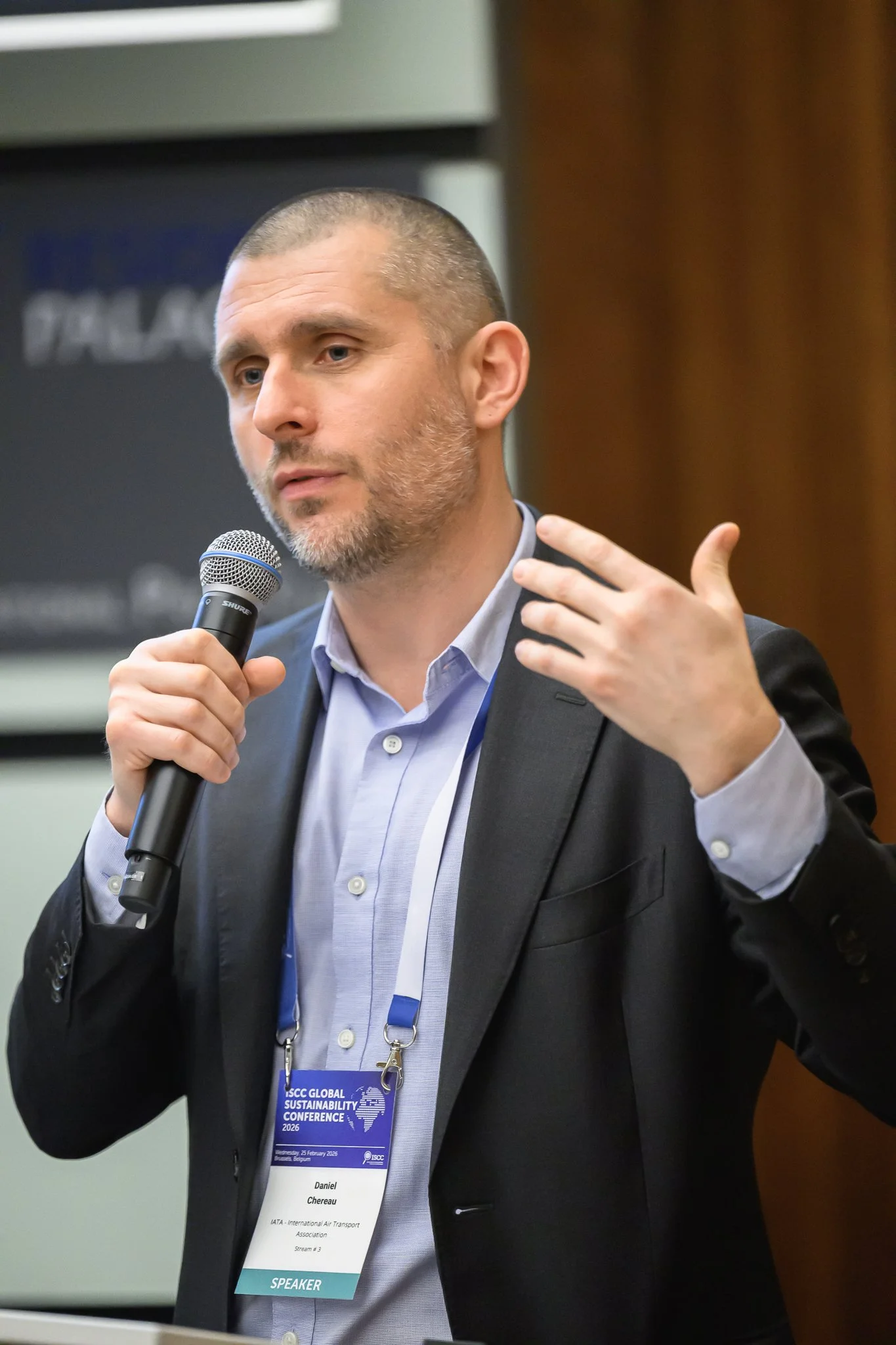 A speaker gestures near his shoulder while holding a microphone.