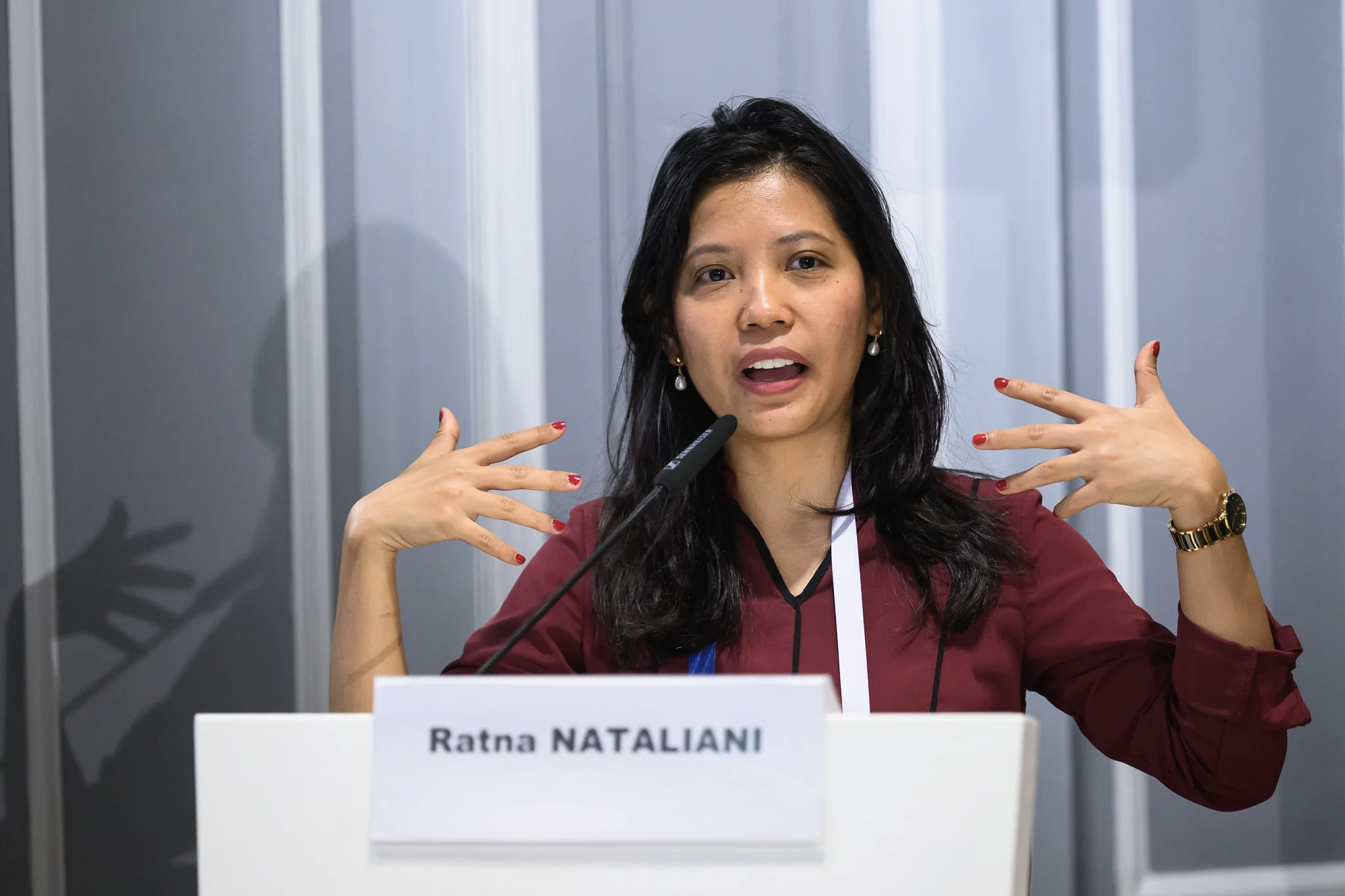 Ratna Natalianti gestures with both hands at a lectern bearing her name.