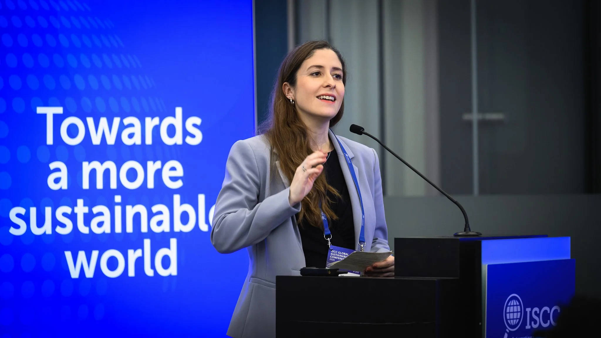 A woman in a light blue jacket smiles and gestures at the lectern.