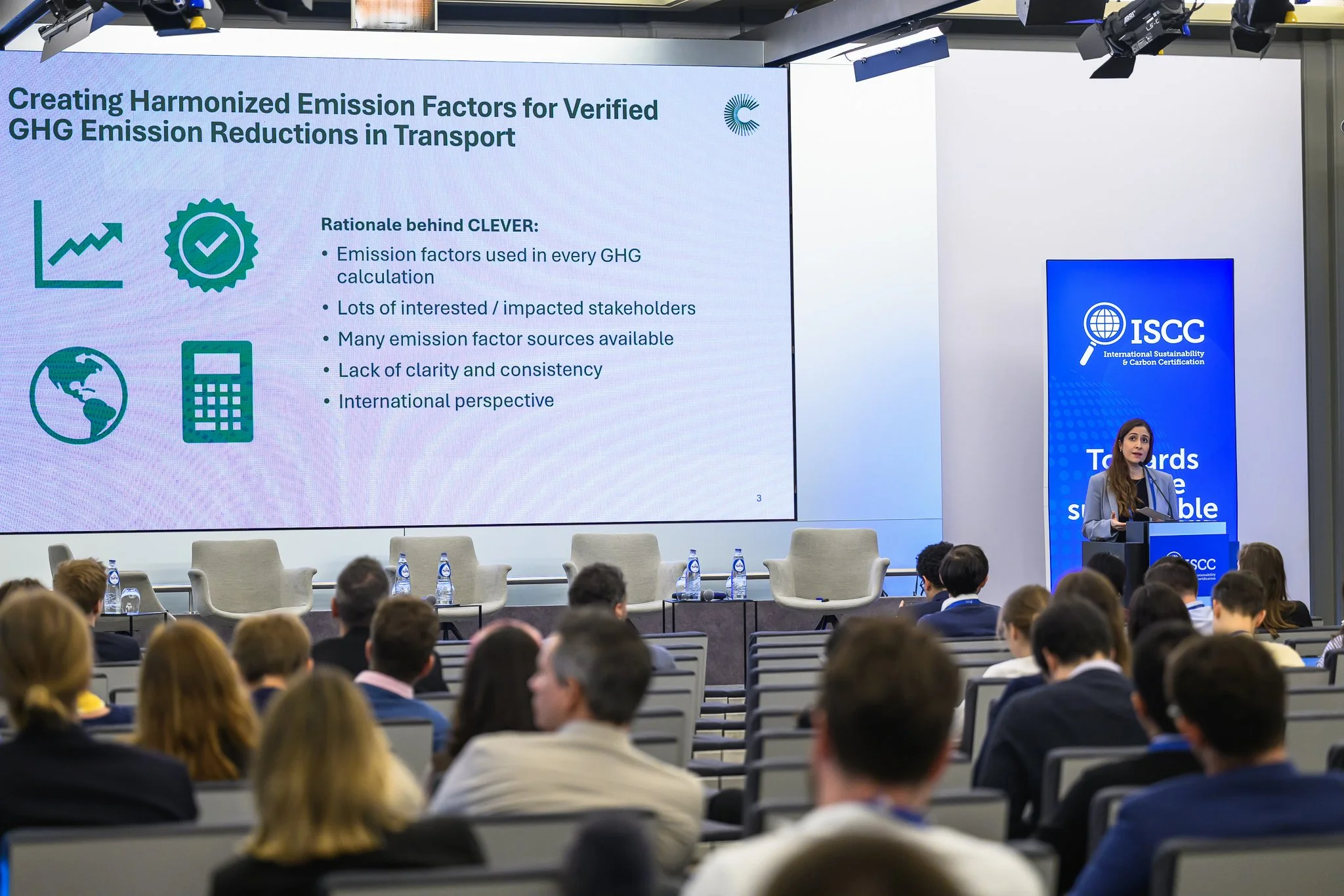 The audience watches a slide about harmonised emission factors and greenhouse gas reductions in transport.