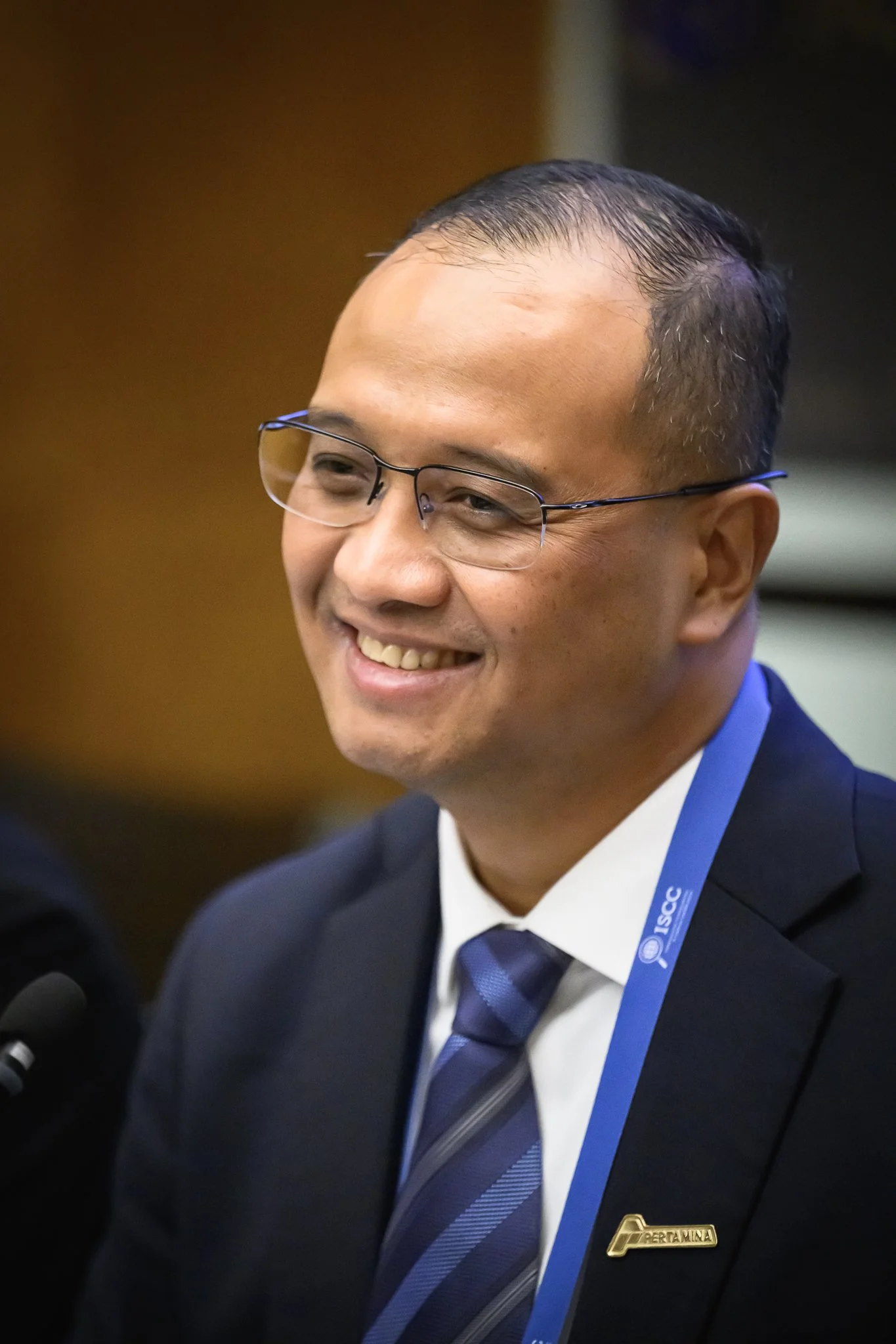 A smiling man with glasses and a blue tie sits at a conference table.