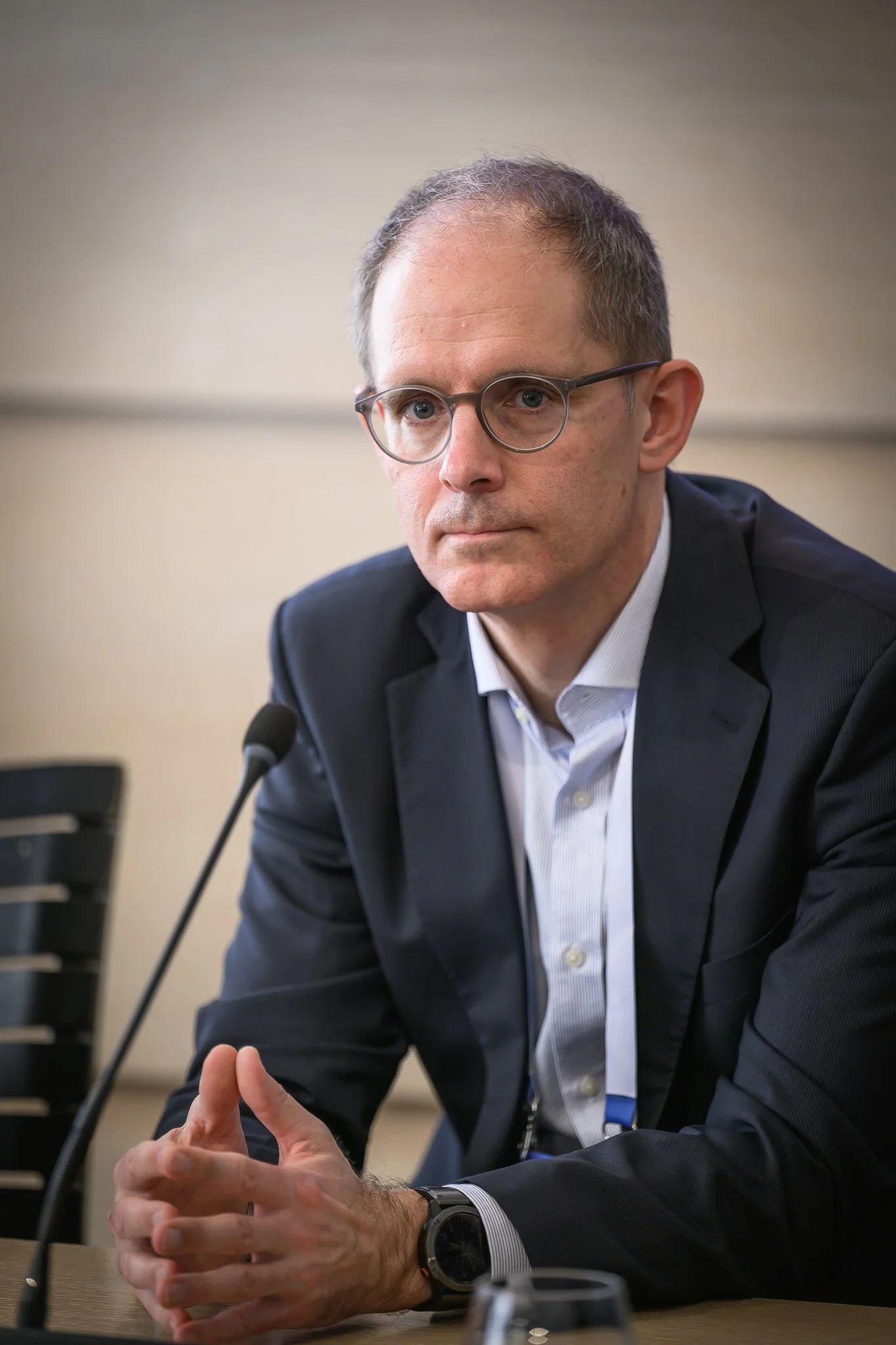 A man with glasses listens with his hands together at a conference table.