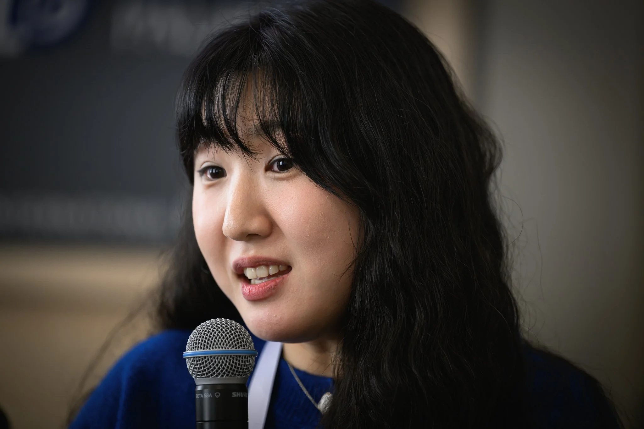 Close-up of a woman with dark hair speaking into a handheld microphone.
