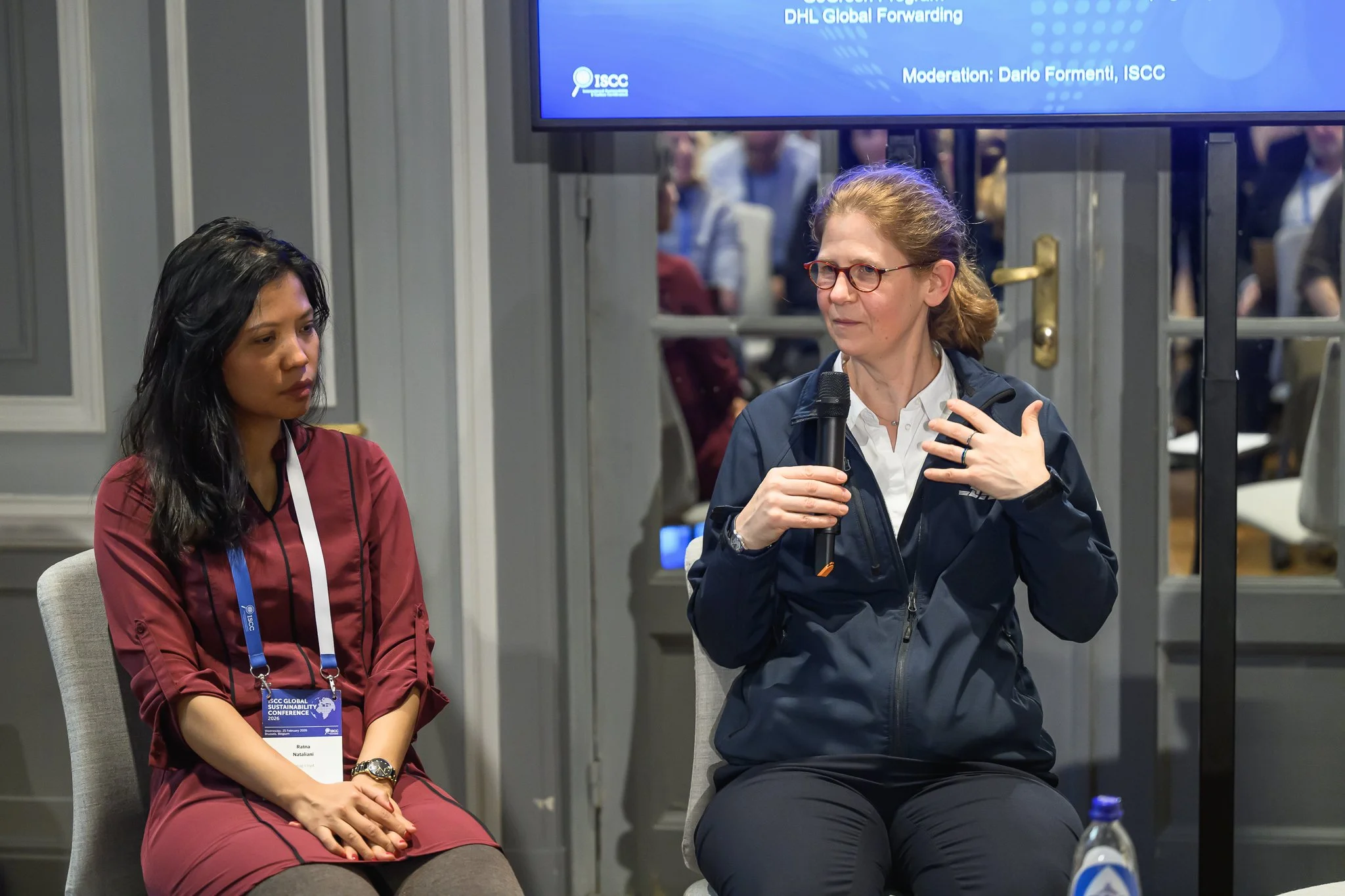 Two women sit together during a discussion, one gesturing while speaking.