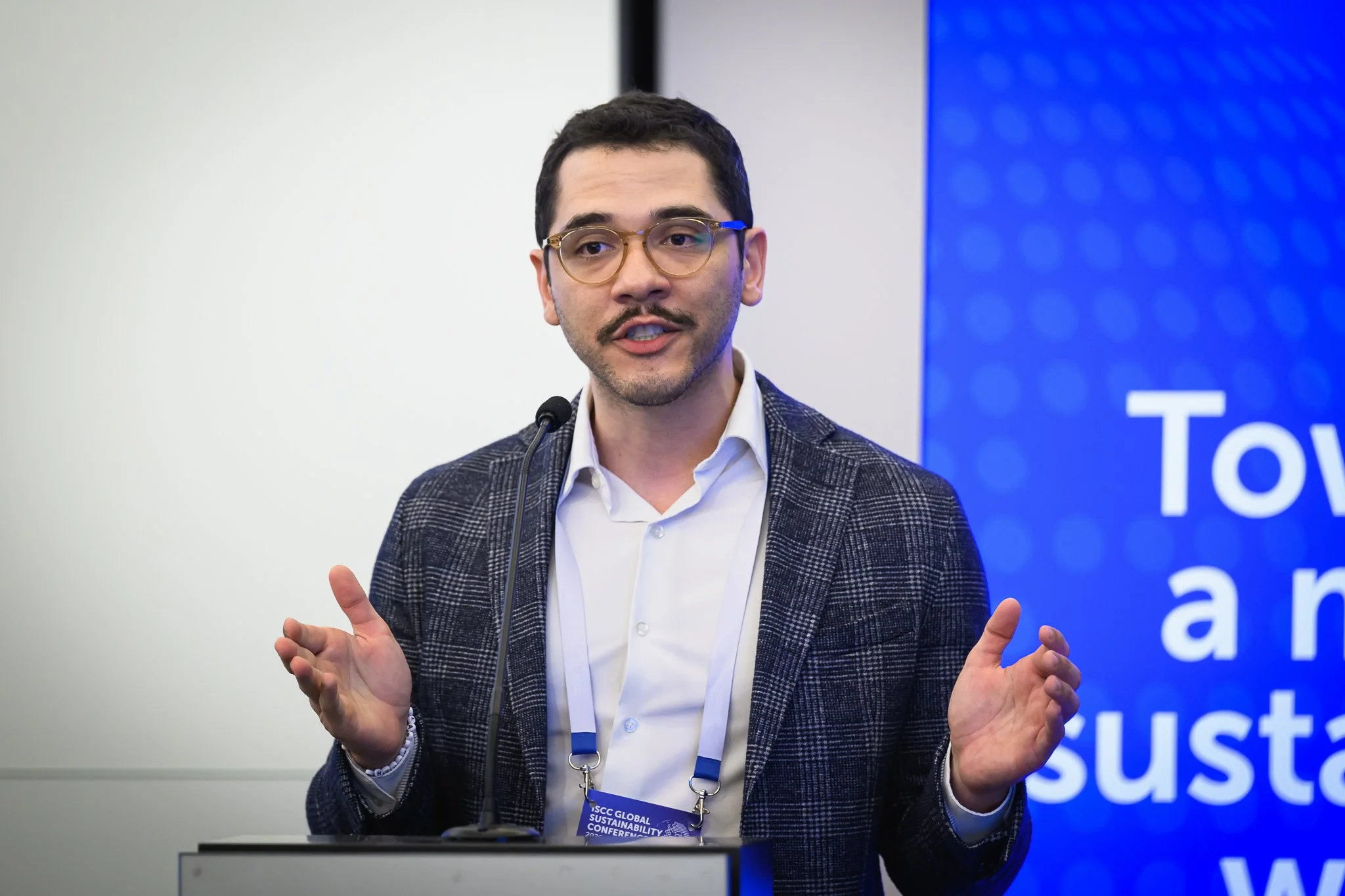 A man with glasses speaks at the lectern with both hands raised.