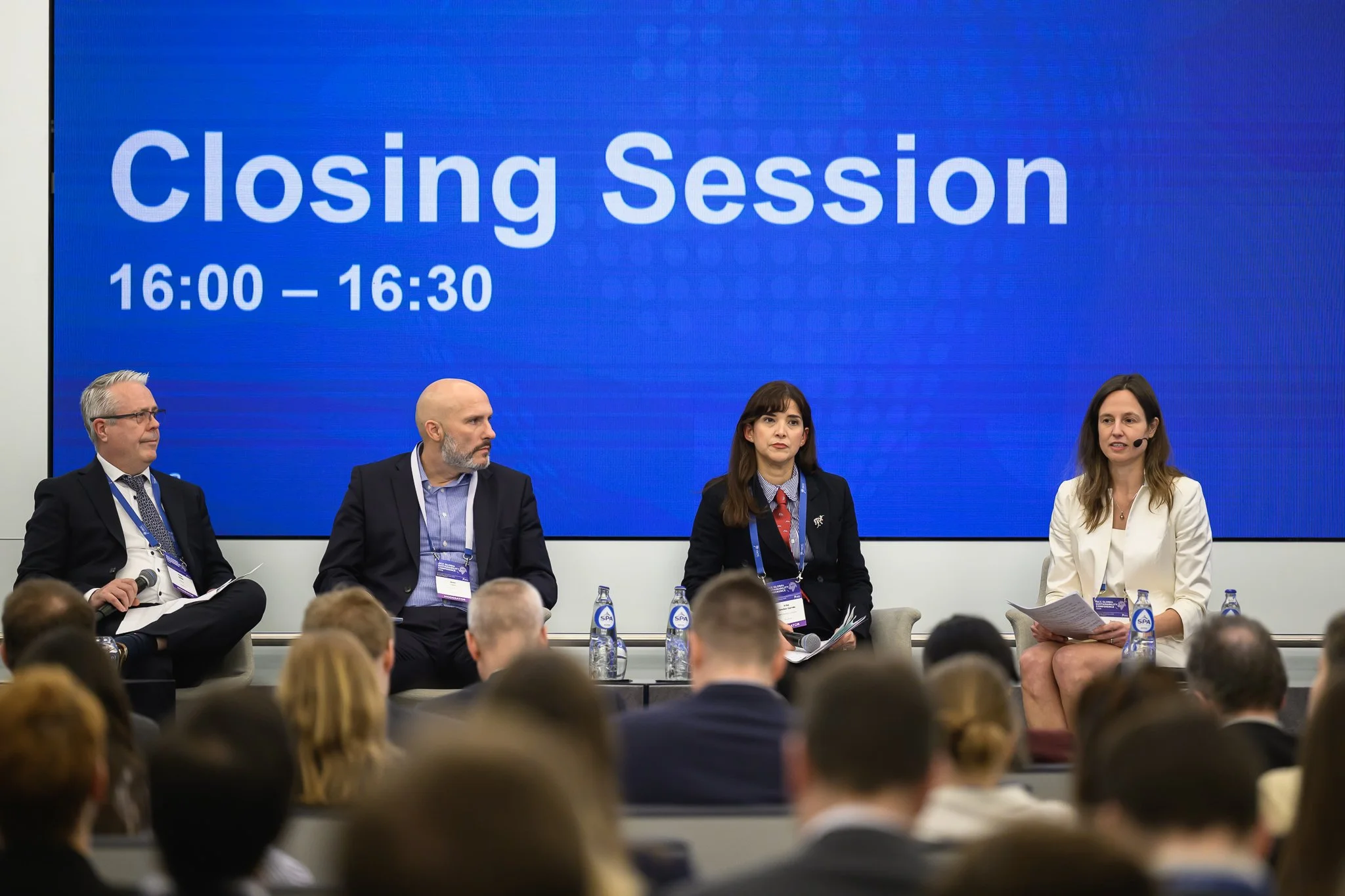 Four participants sit on stage beneath a screen reading Closing Session.