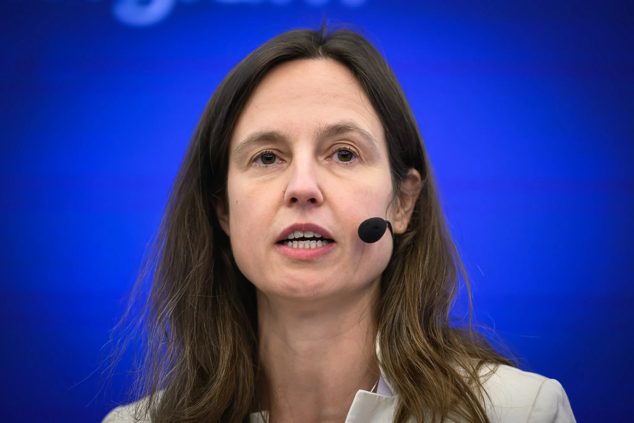 Close-up of a woman wearing a headset microphone against a blue background.