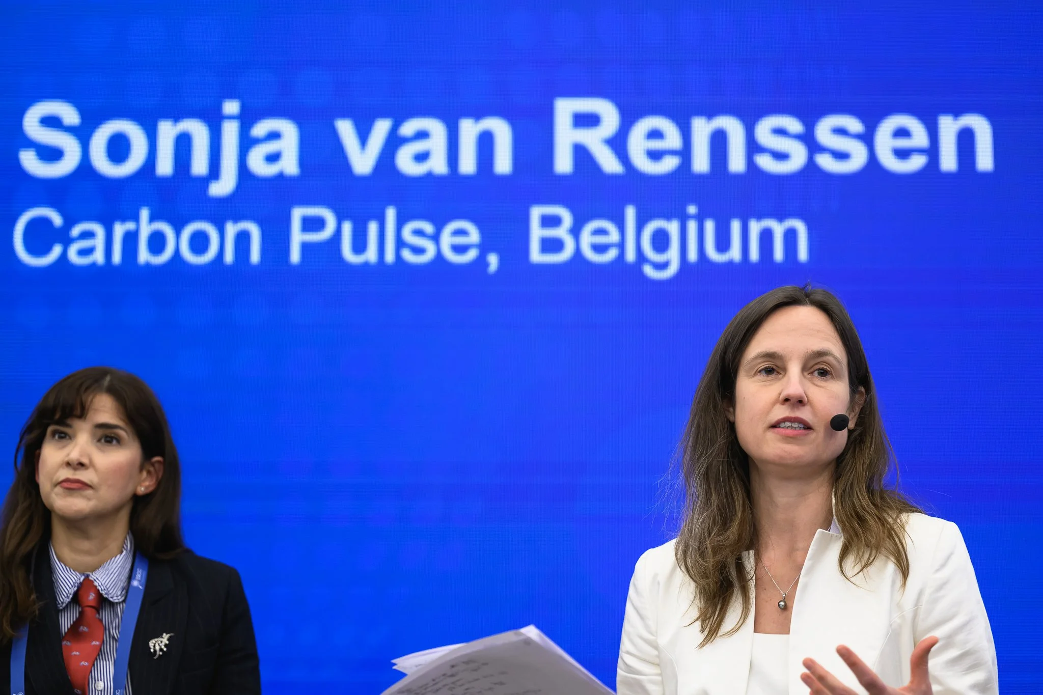 Two women sit on stage while the moderator addresses the audience.