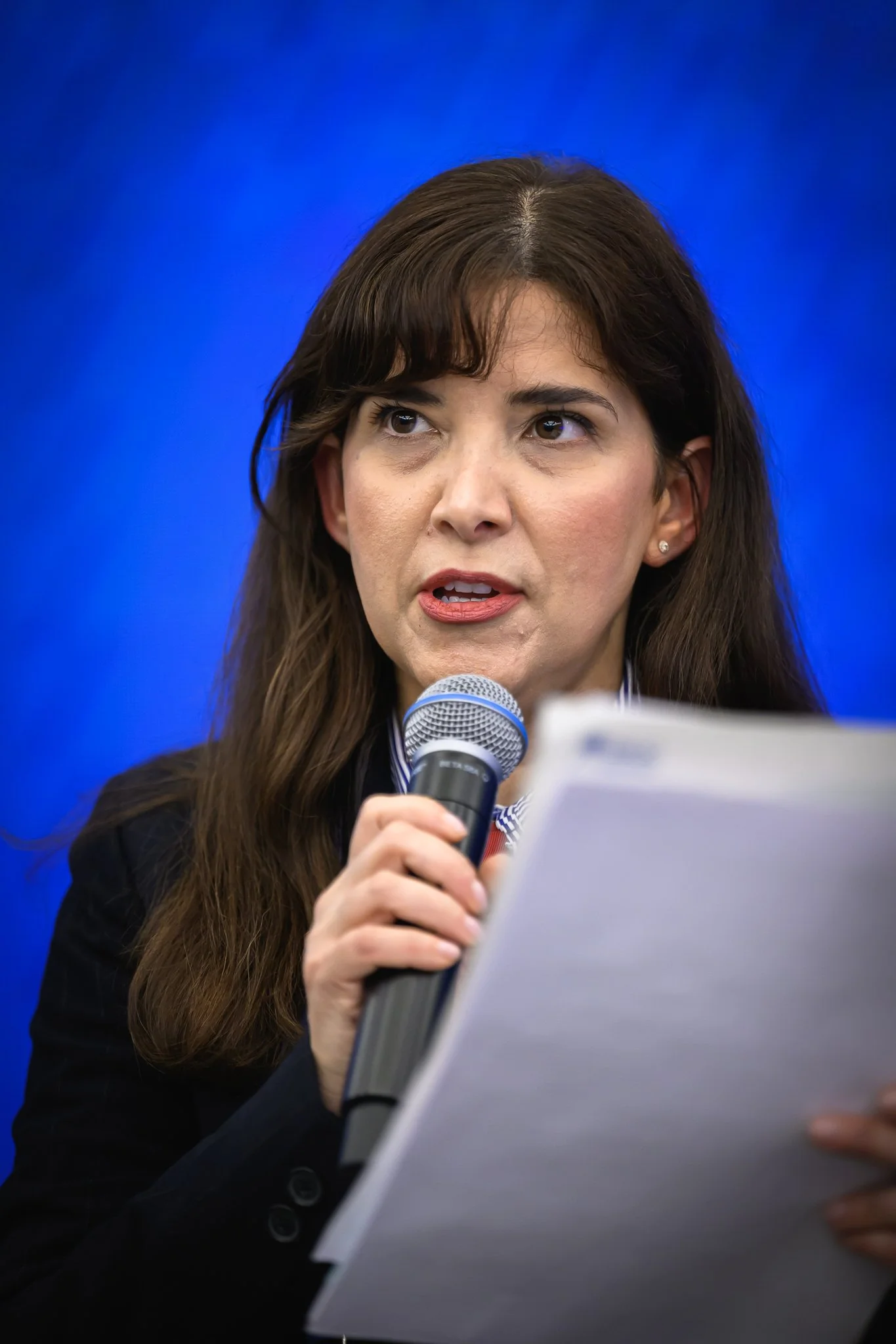 Close-up of a woman reading notes while speaking into a microphone.