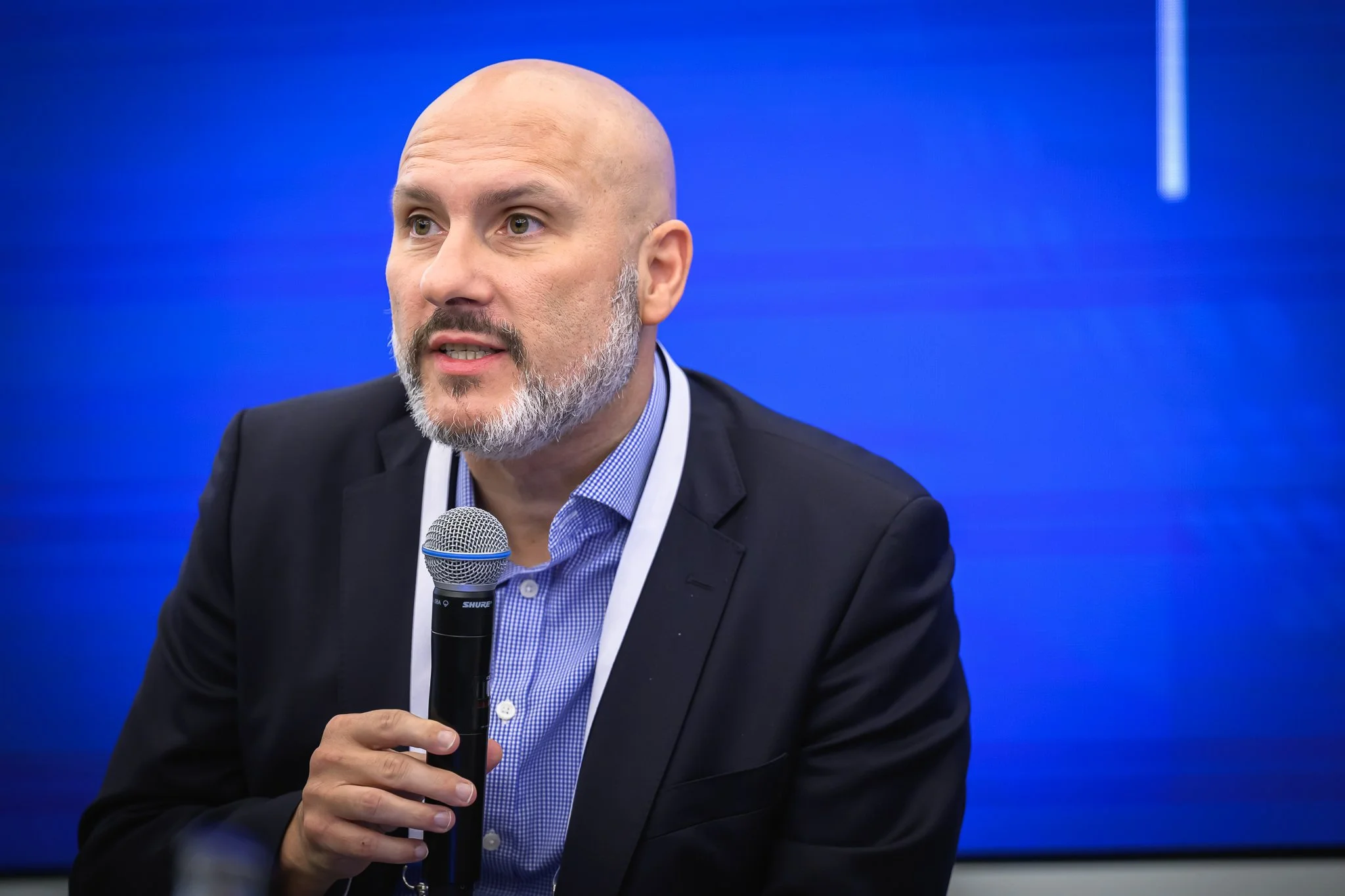 A bald man with a grey beard holds a microphone during the closing panel.