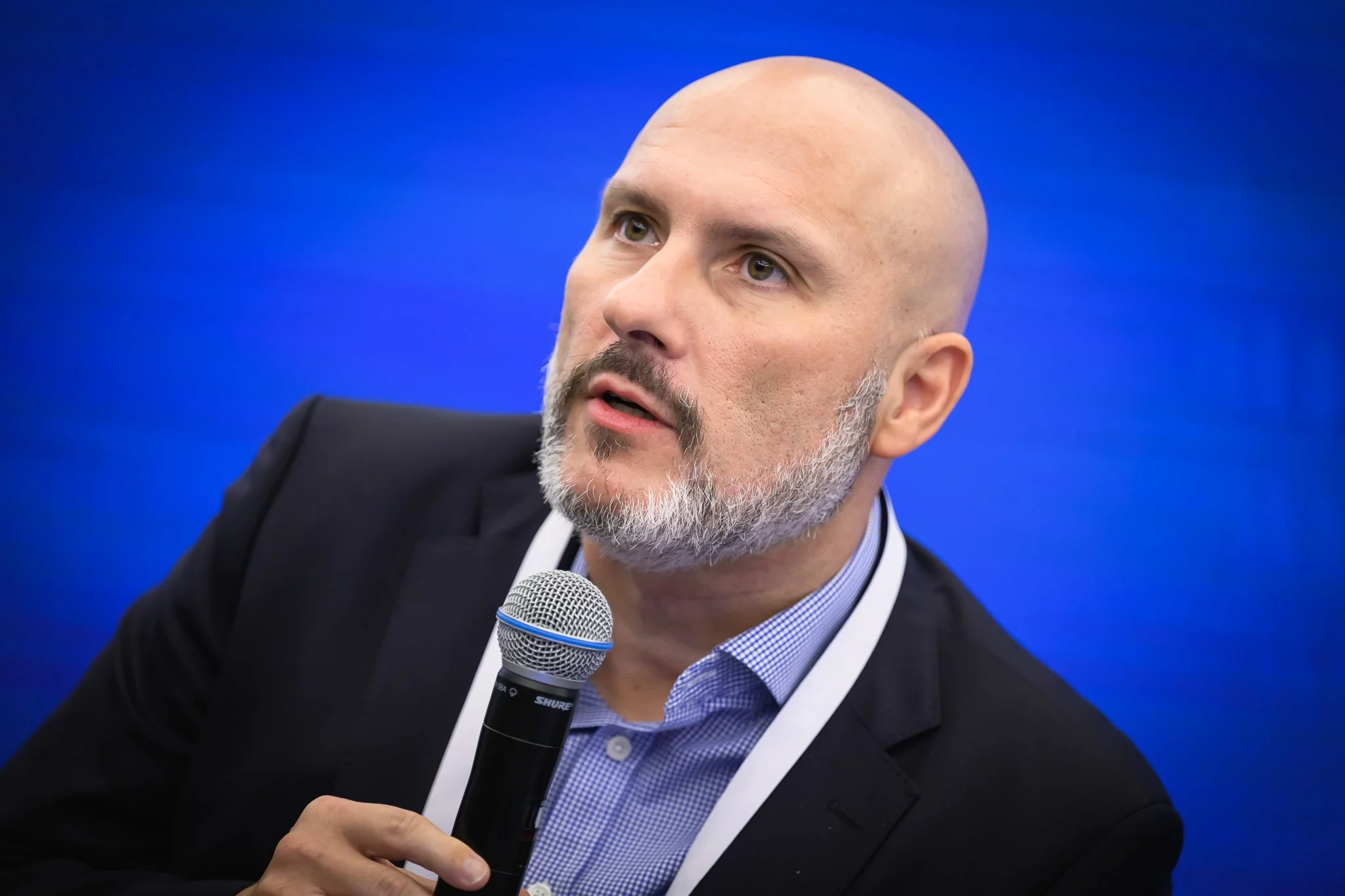 Close-up of a bald panel participant speaking into a handheld microphone.