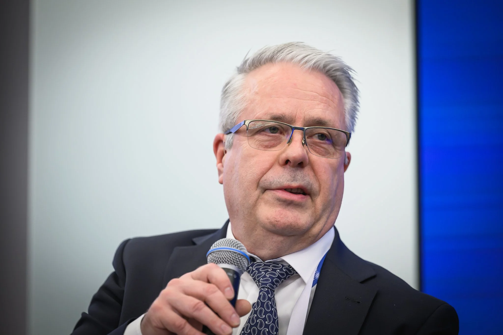 An older man with glasses holds a microphone during the closing panel.