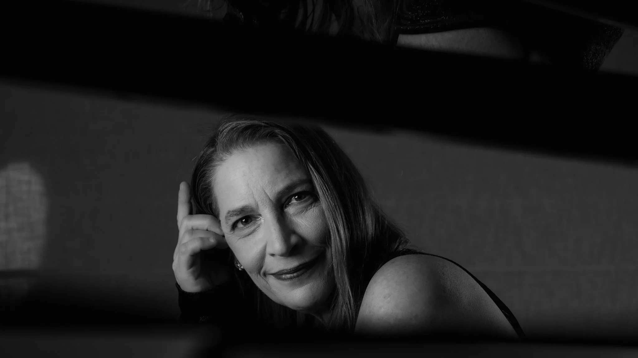 Photo en noir et blanc de Nadia Weintraub souriante regardant vers l'objectif, avec un bras posé sur un coussin ou une banquette, prise de vue en contre-plongée.