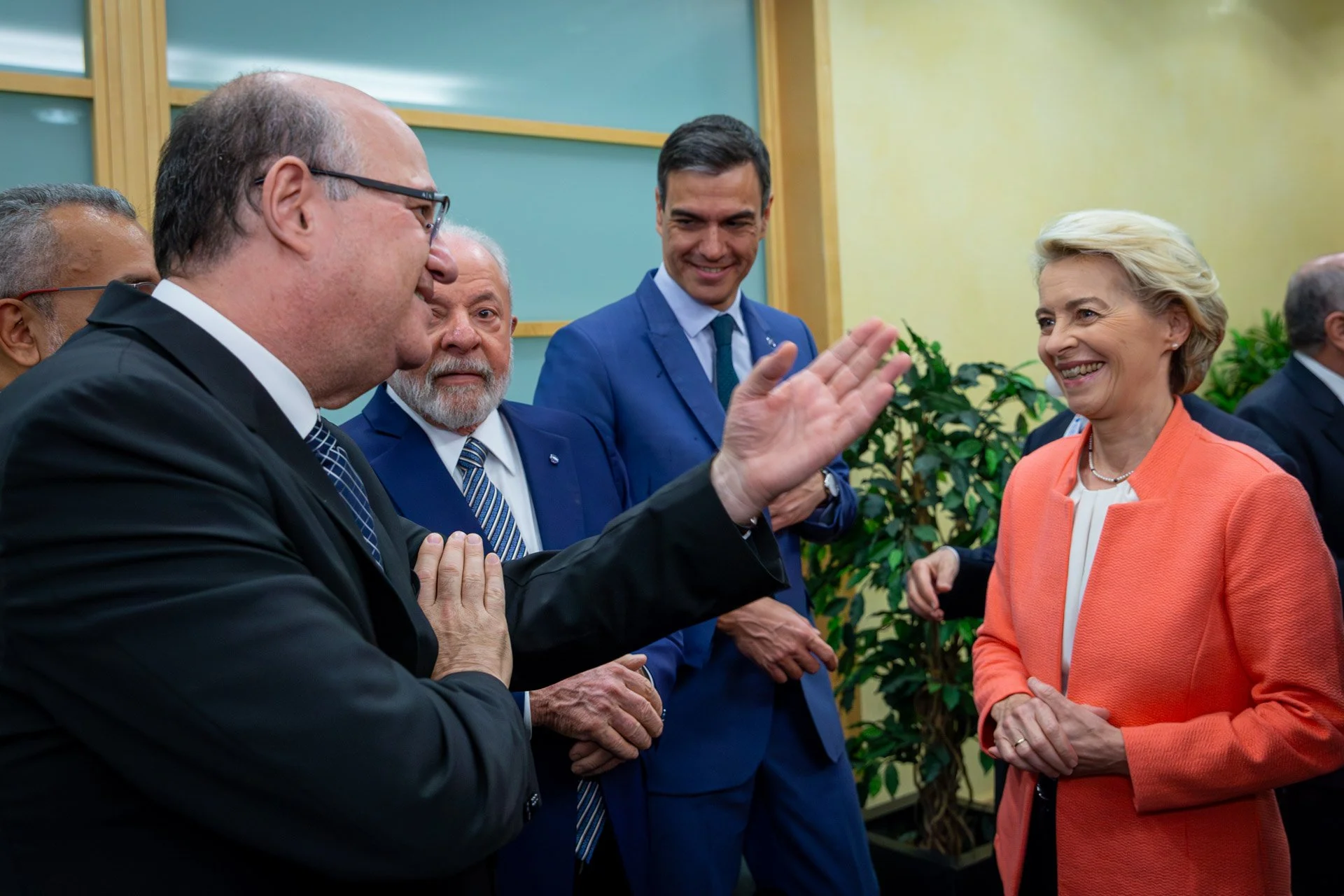 Groupe de personnes en costume discutant et souriant dans un cadre professionnel, devant des plantes.