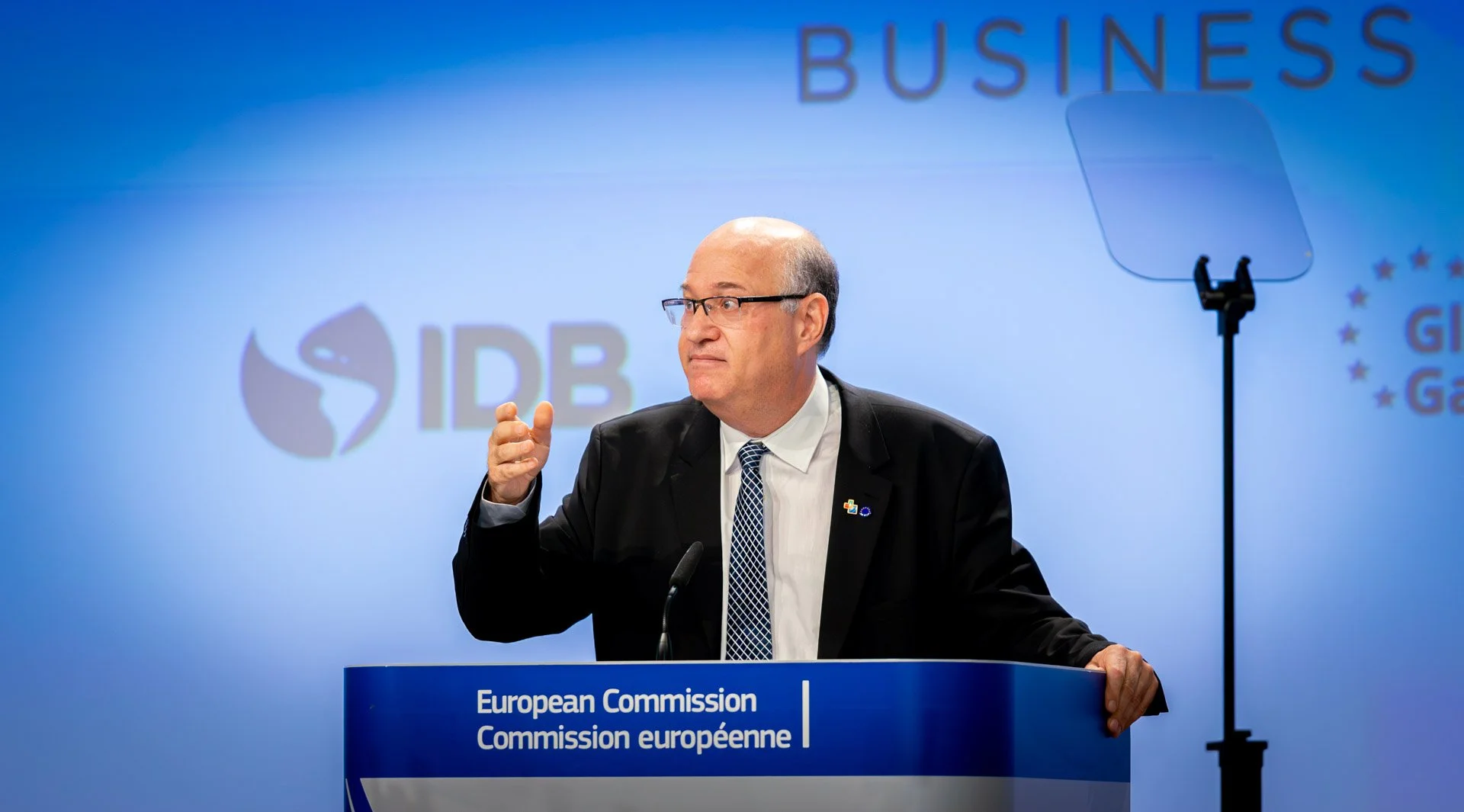 Homme en costume parlant à un podium de la Commission européenne avec logos en arrière-plan.