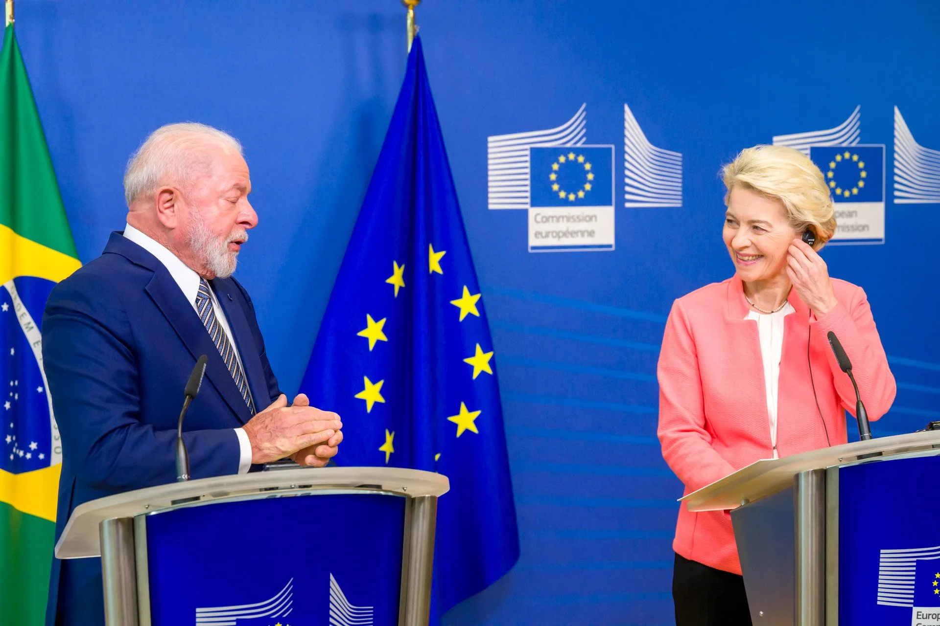 Deux personnes discutent devant des pupitres avec les drapeaux de l'Union européenne et du Brésil, fond Commission européenne.