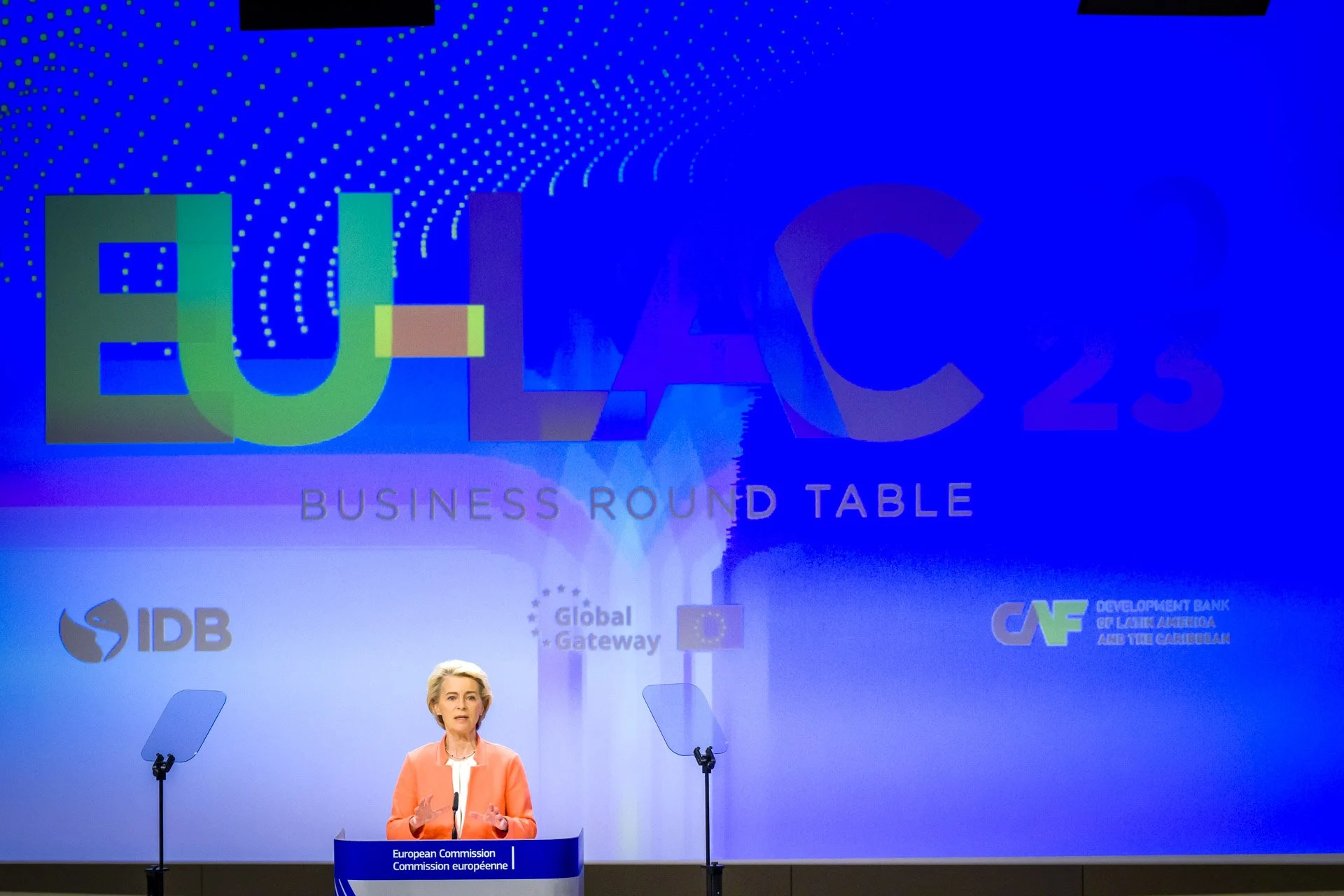 Une conférence intitulée "EU-LAC 2023 Business Round Table" avec une personne parlant à un podium de la Commission européenne, sur fond bleu avec des logos de l'IDB, Global Gateway et CAF.