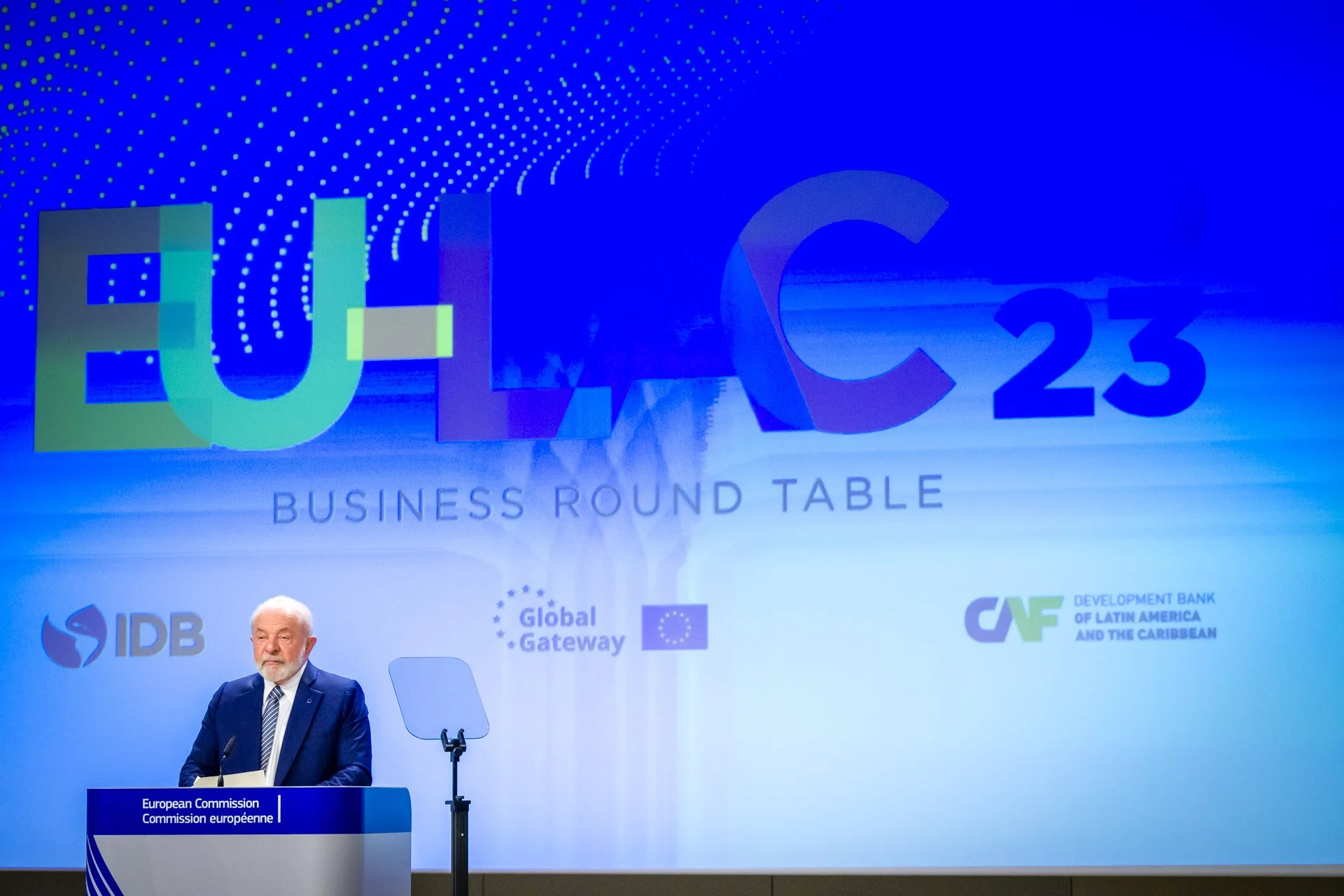 Un homme parlant à un podium lors de la conférence EU-LAC 23, avec des logos d'organisations comme la Commission européenne, IDB, Global Gateway, et le CAF en arrière-plan.