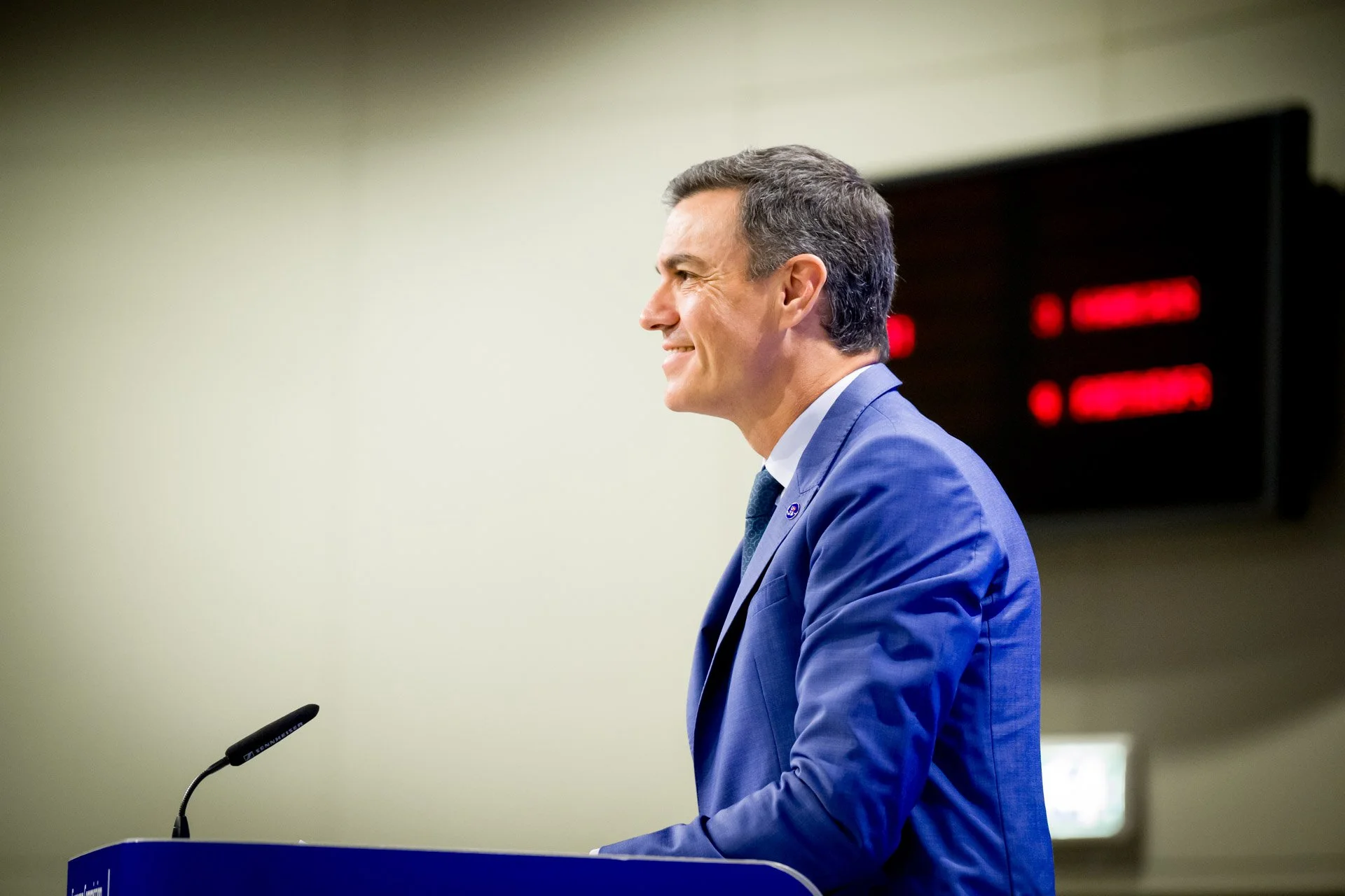 Homme en costume bleu parle à un podium avec un microphone.