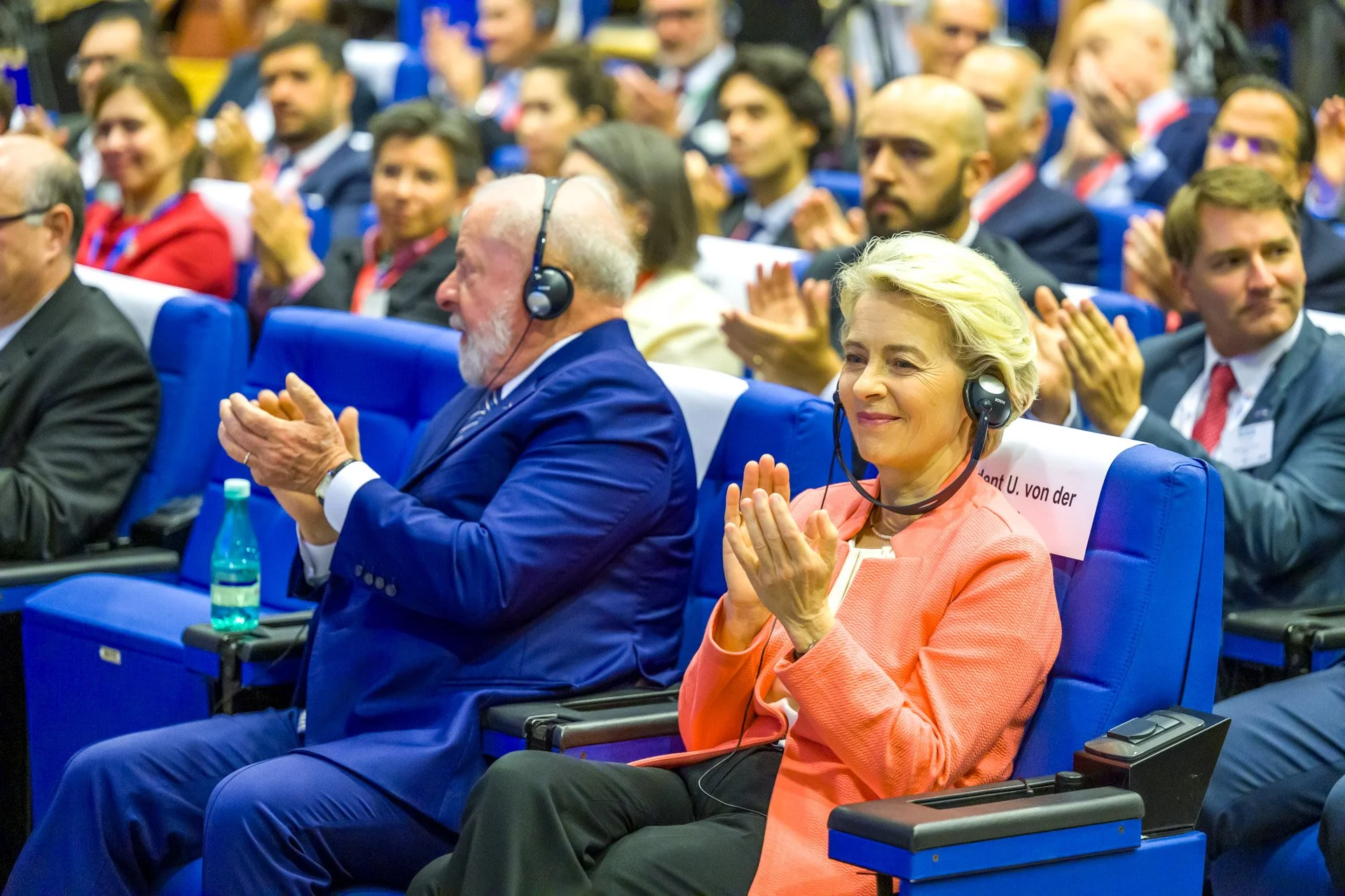 Personnes applaudissant lors d'une conférence, avec des casques d'écoute."}