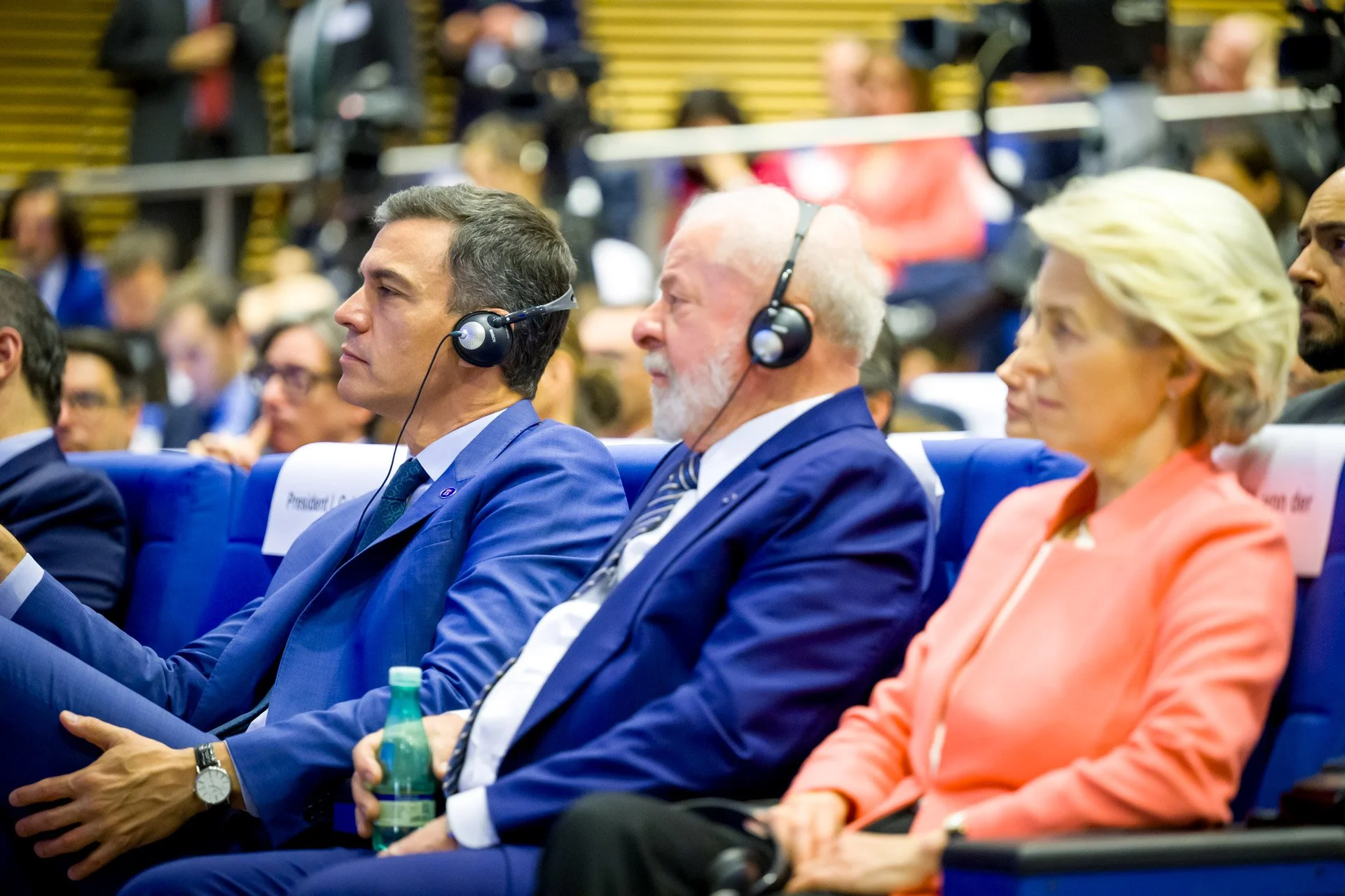 Personnes assises lors d'une conférence, portant des casques audio, arrière-plan flou.