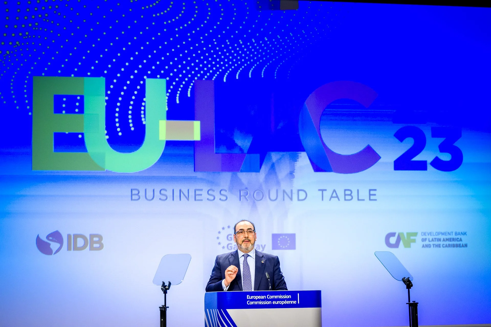 Un homme en costume se tient derrière un podium lors d'une conférence intitulée "EU-LAC 23 Business Round Table". En arrière-plan, le logo de la Commission européenne et les logos d'organisations telles que la Banque interaméricaine de développement