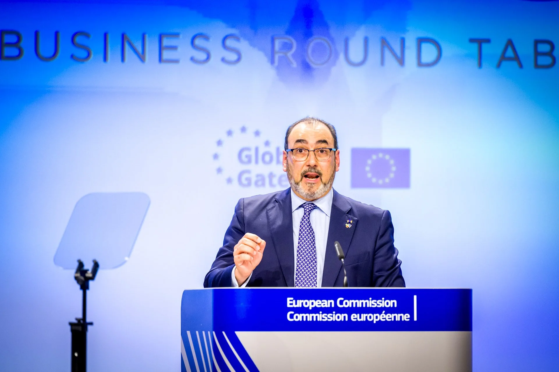 Homme en costume s'exprimant à un pupitre lors d'un événement de la Commission européenne, avec logos "Global Gateway" et drapeau de l'UE en arrière-plan.