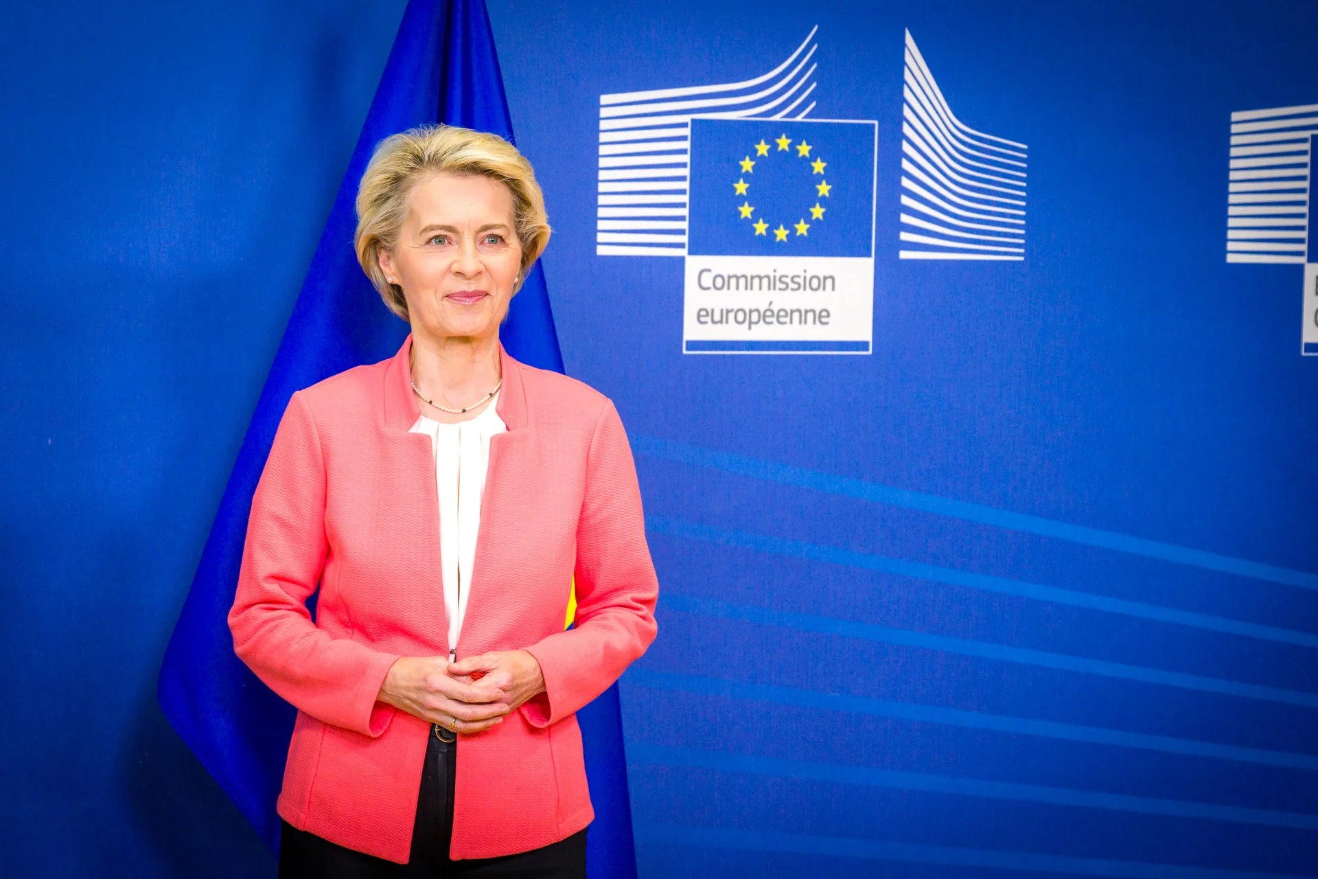 Femme devant un fond avec le logo de la Commission européenne et un drapeau bleu.
